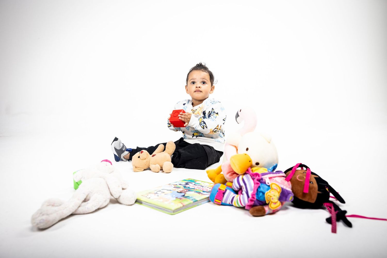 Child sitting among stuffed animals and toys on white background.