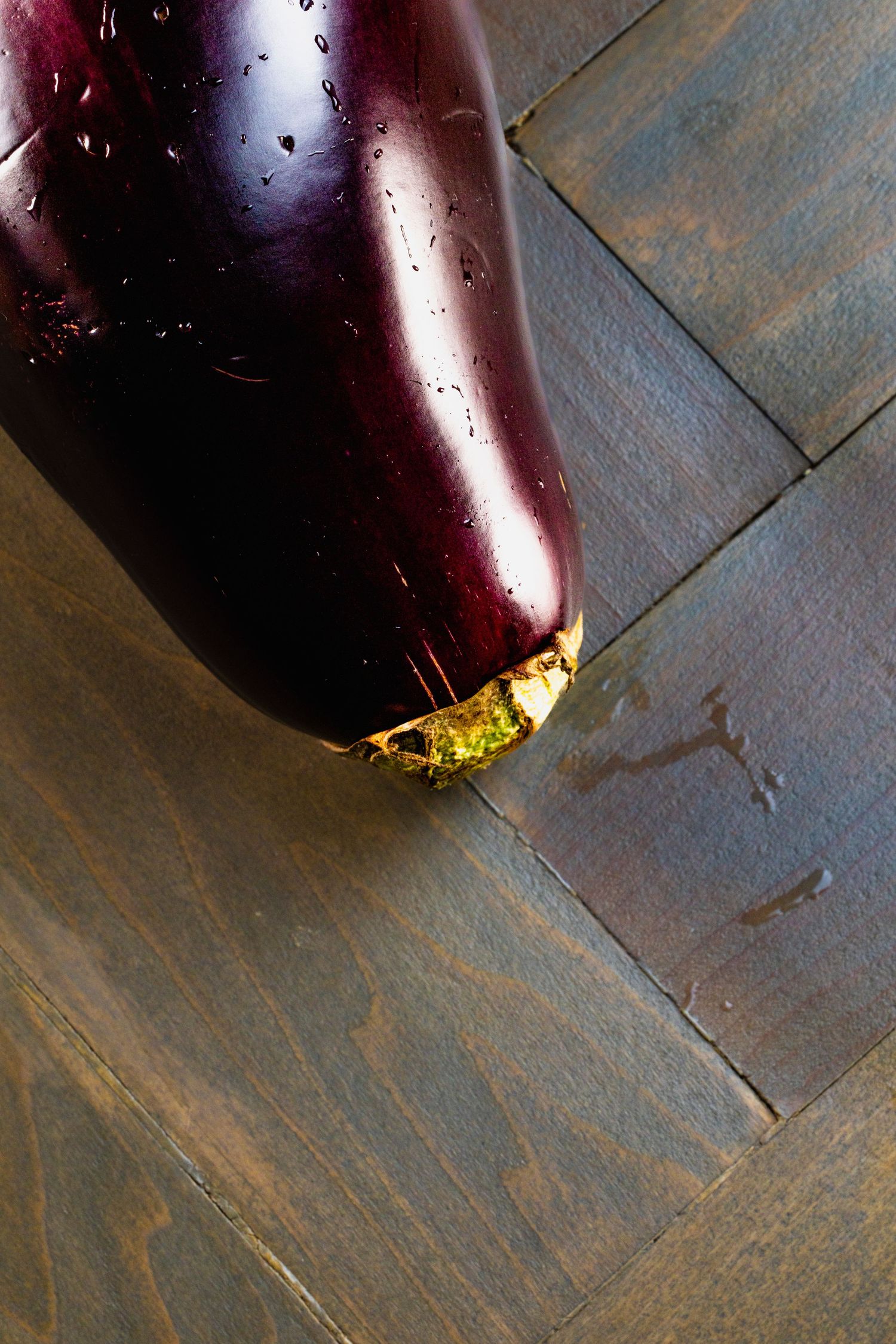Large fresh eggplant on dark wooden surface with golden edges reflecting light.