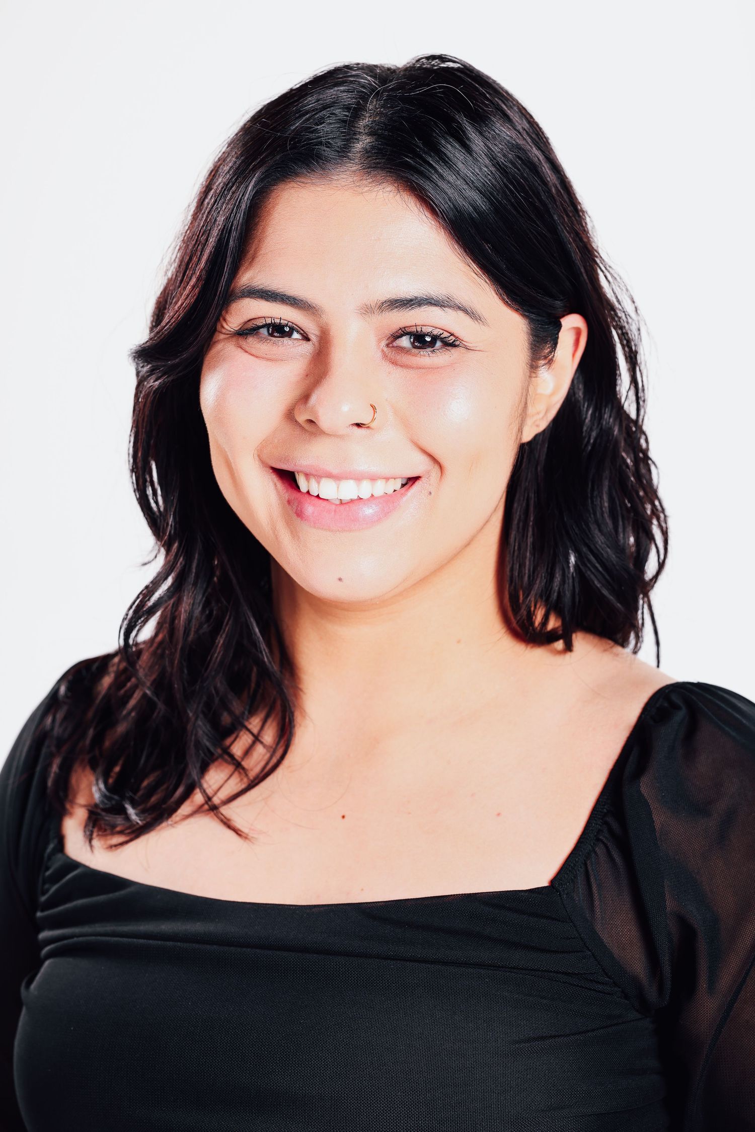 Professional headshot against white background showing a warm smile and dark wavy hair, wearing a black top.