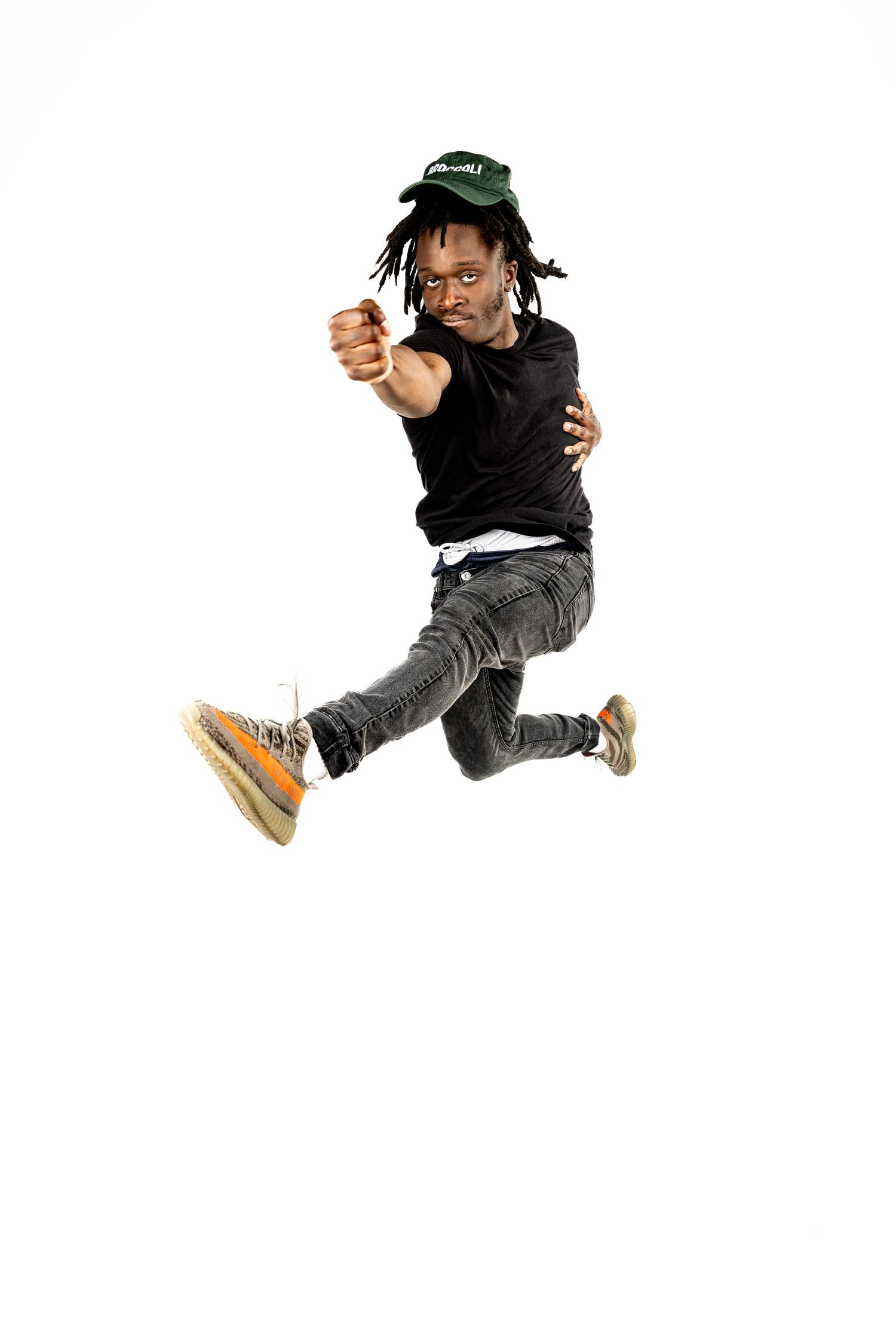 Person in black outfit and cap jumping energetically against white background.