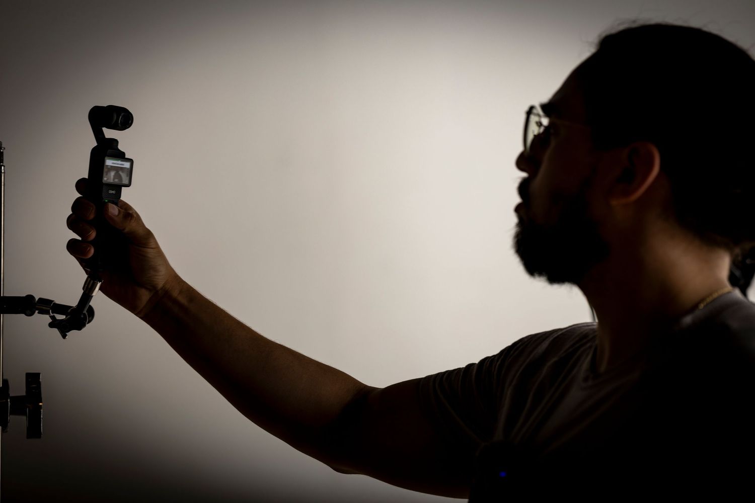Silhouetted person holding up a camera gimbal stabilizer against a light background.
