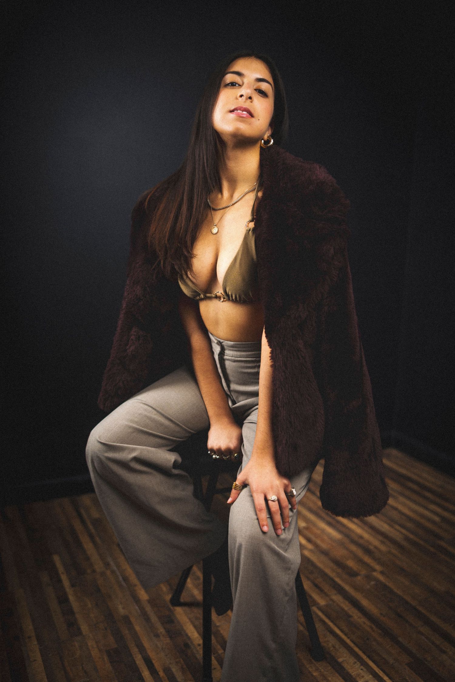 Model wearing brown fur coat and gray pants poses dramatically on wooden floor.