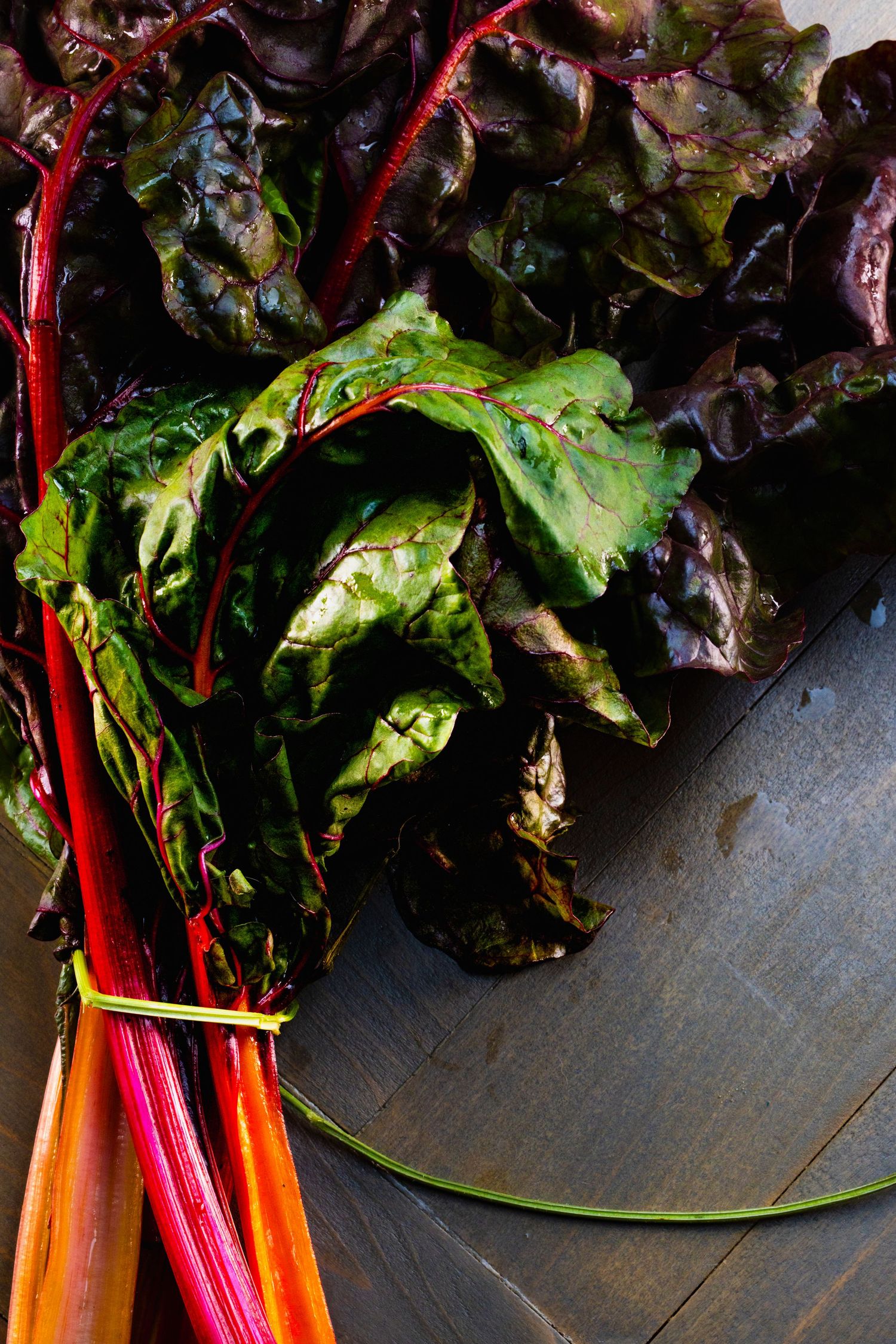 Vibrant red chard leaves and stems arranged on a rustic wooden surface.