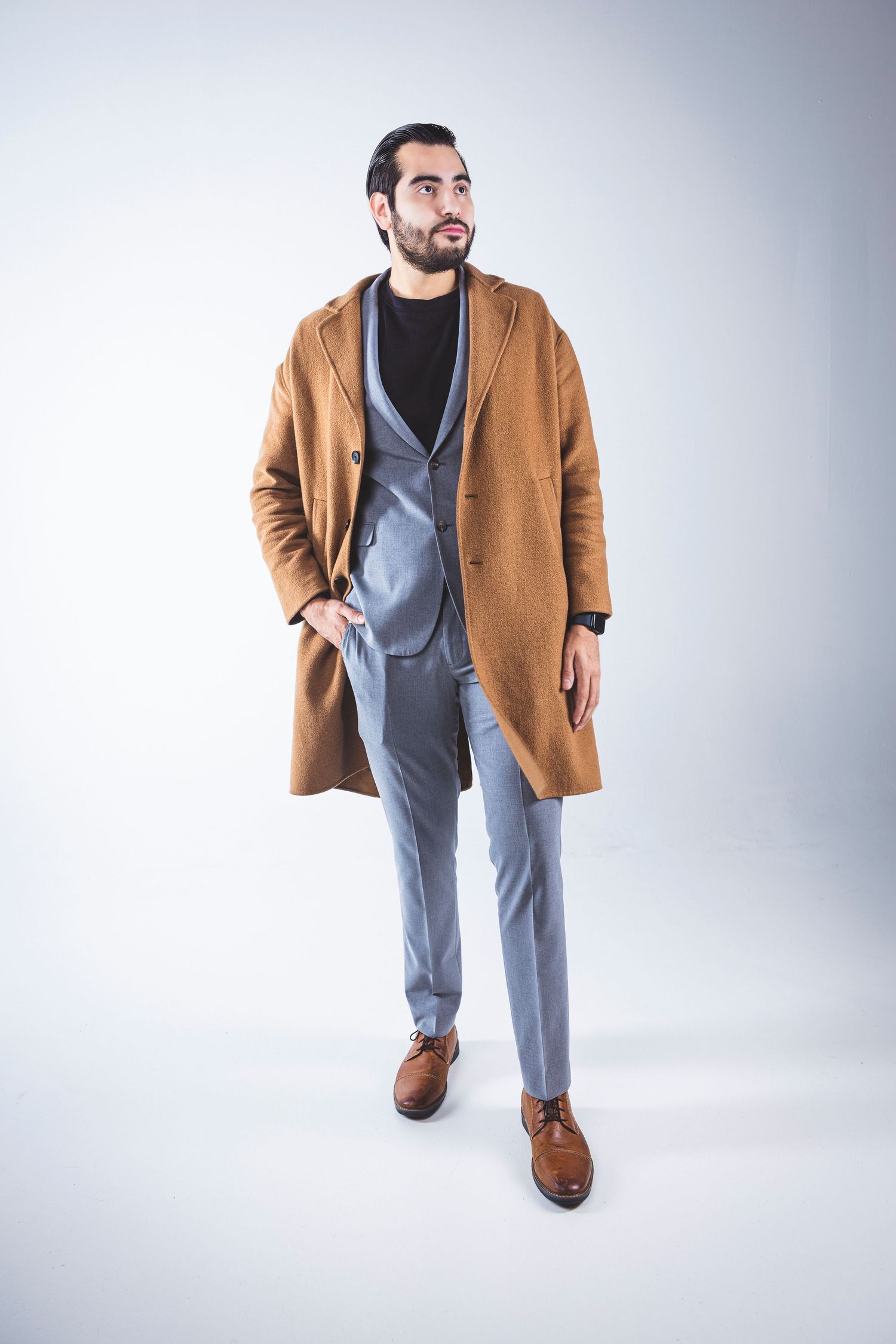 Man models camel coat over gray suit in professional studio photoshoot.