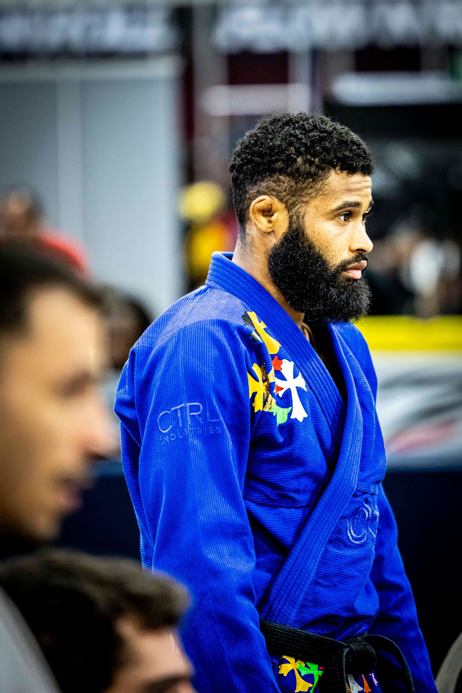 Competitor stands focused in blue competition gi with patches and black belt.