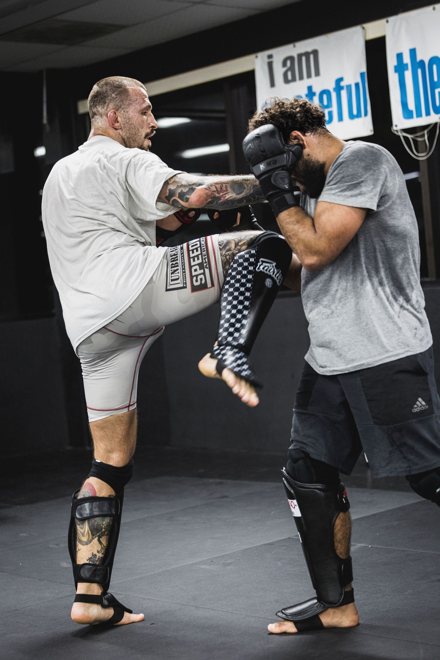 Two mixed martial arts fighters sparring in a gym, with one executing a powerful high kick during training.
