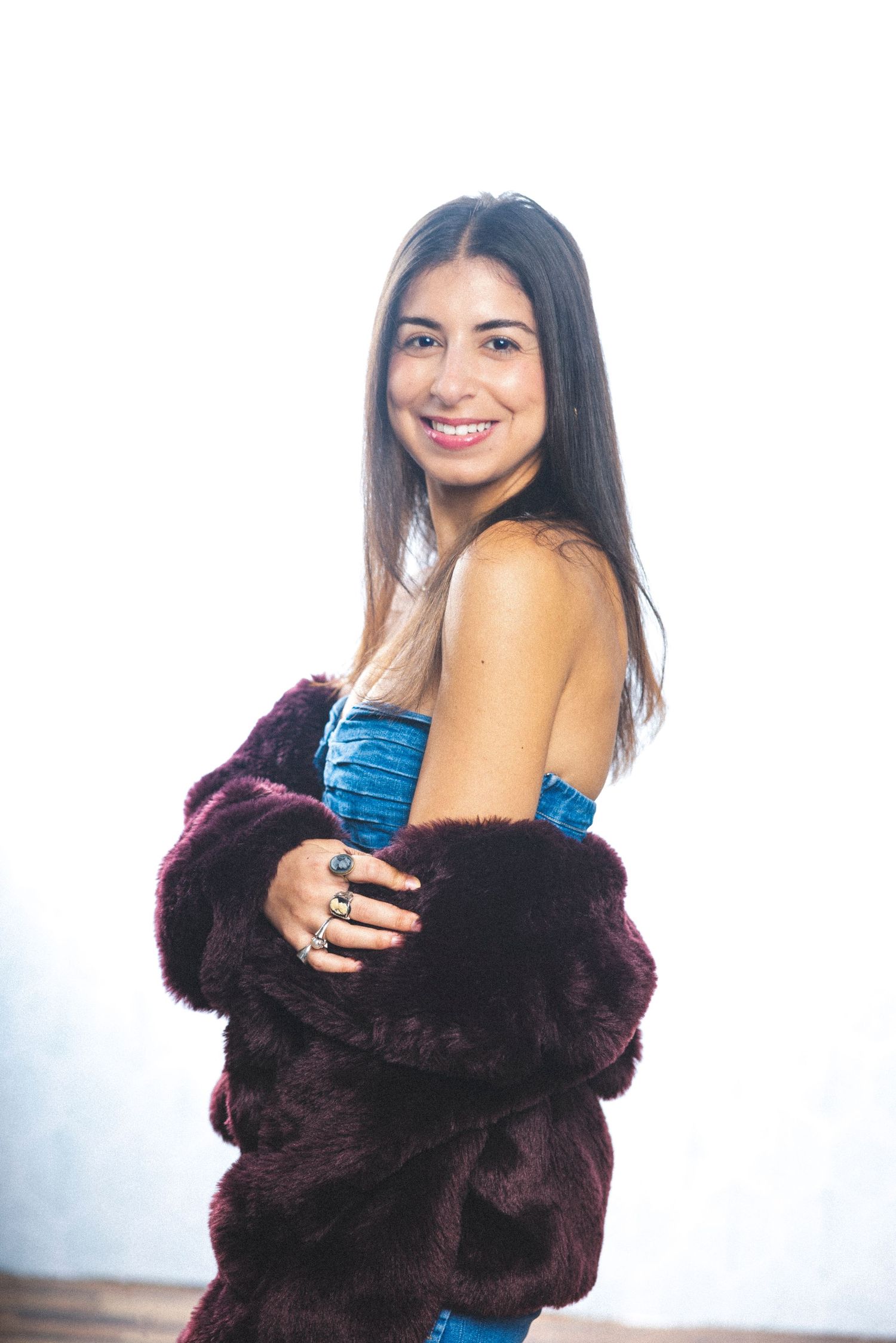 Fashion model in brown fur coat and blue dress poses elegantly in studio setting.