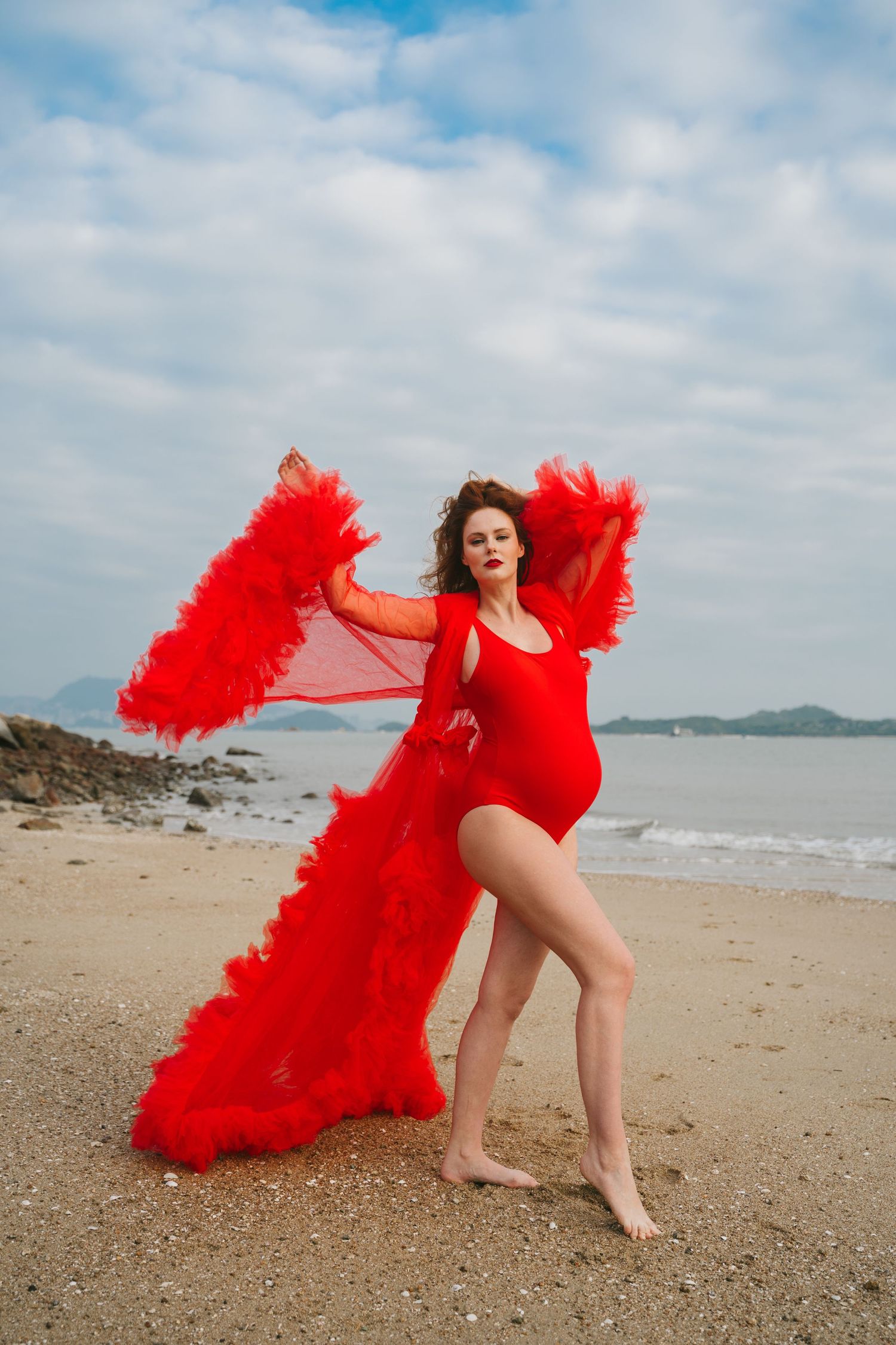 Dancer-like pose on beach featuring red swimsuit and billowing red tulle cape.