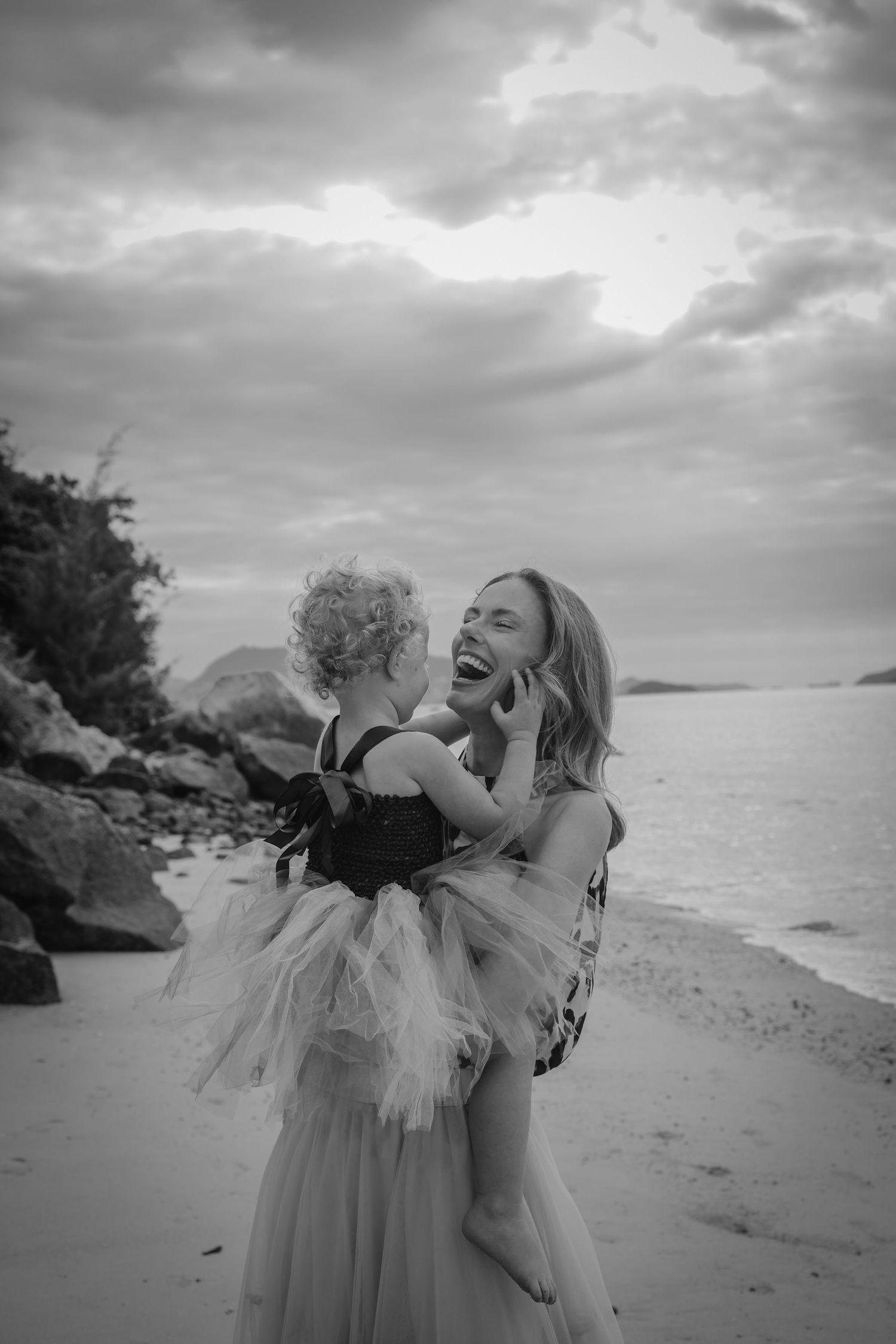 People in ethereal dresses dance along a scenic beach with dramatic clouds overhead.