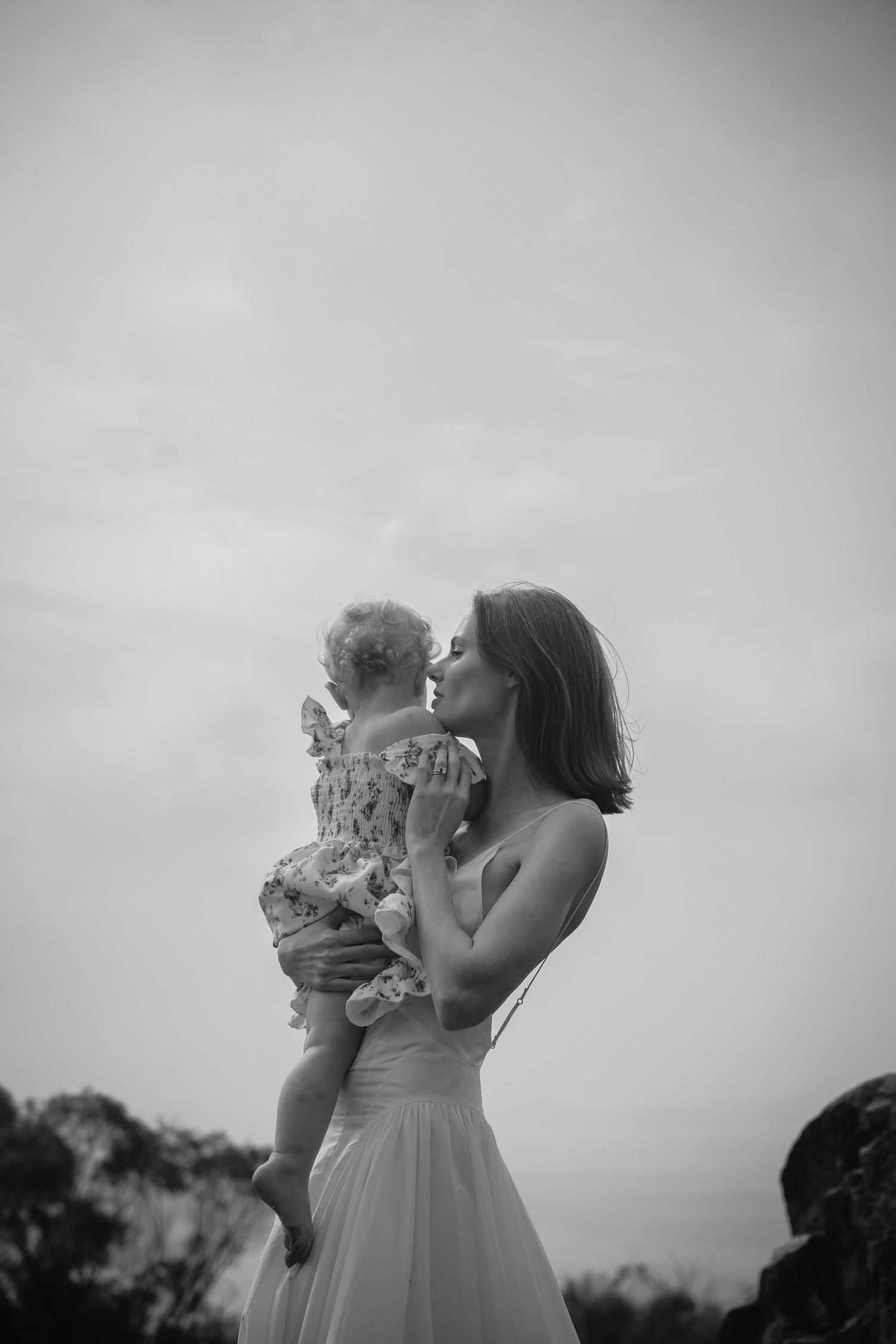 Two people in white dresses share a joyful moment together on a cloudy day.