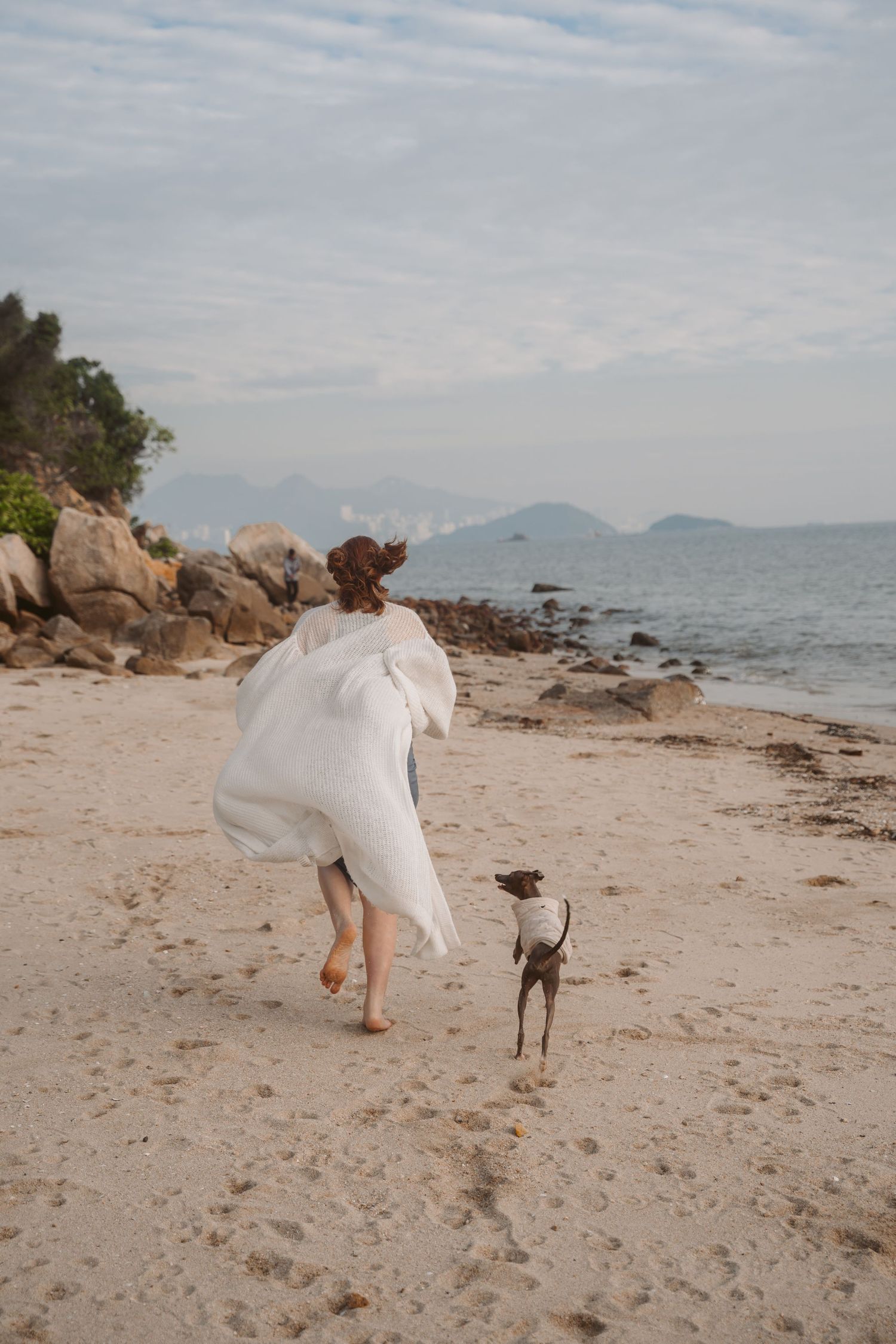 Person in flowing white dress running on beach with Italian Greyhound companion.