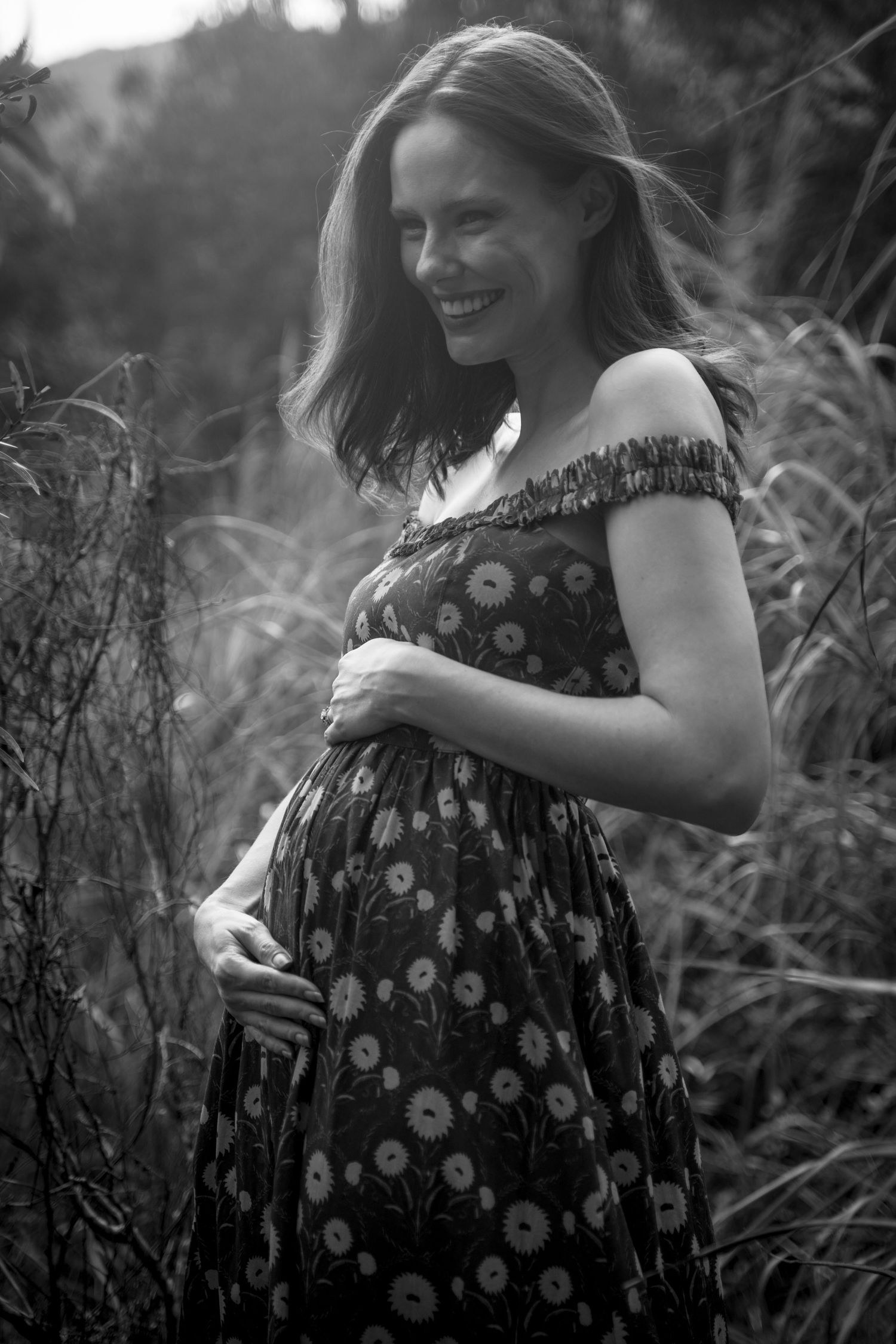 Gentle maternity moment captured in black and white among wild grasses.