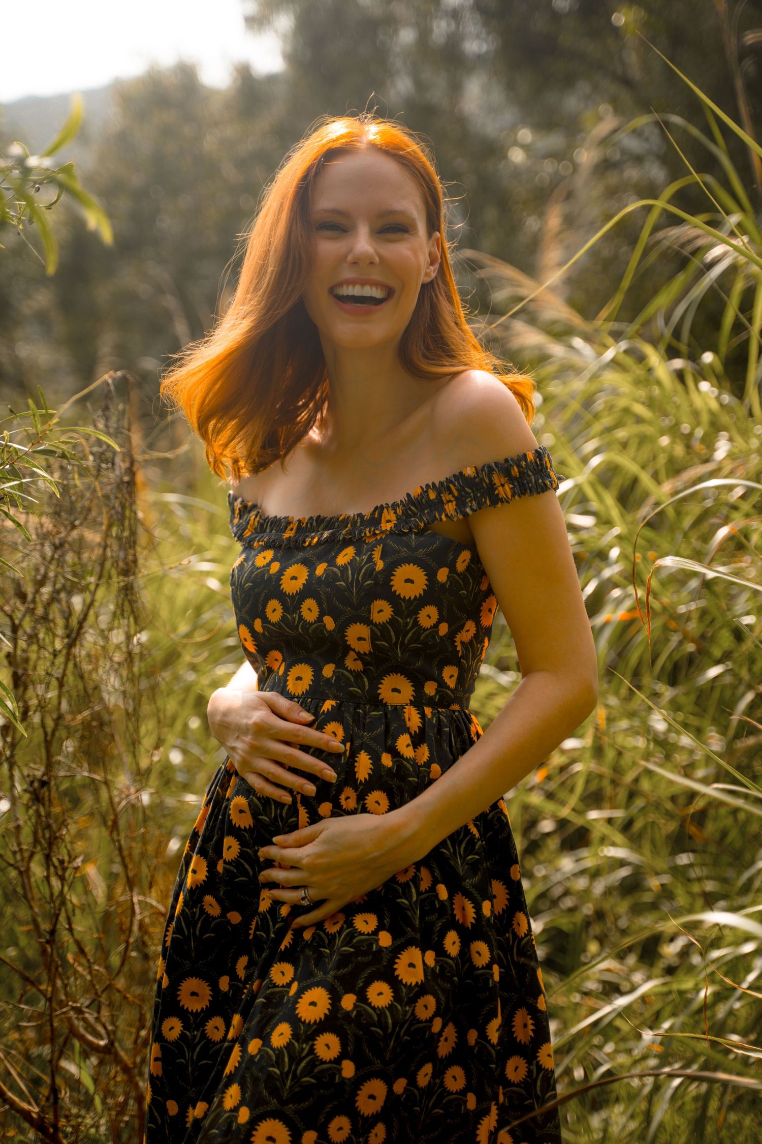 Joyful maternity moment captured in warm sunlight among wild grasses.