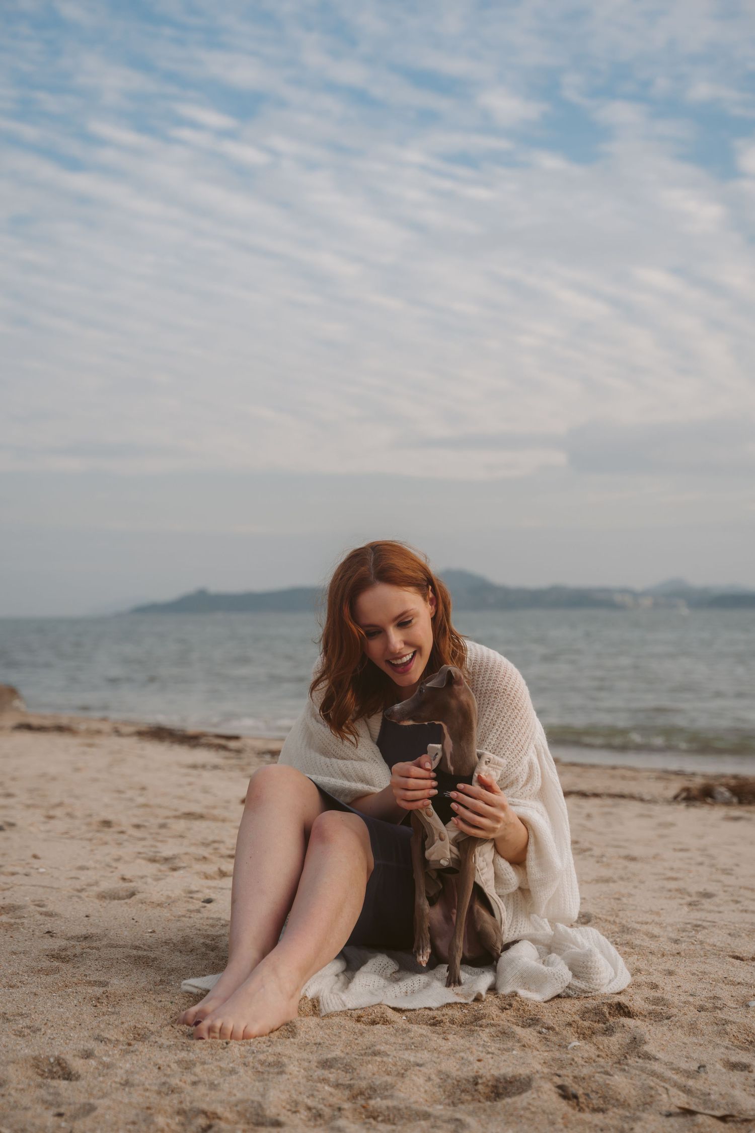 A joyful moment shared between a woman and her Italian Greyhound dog on a peaceful beach.