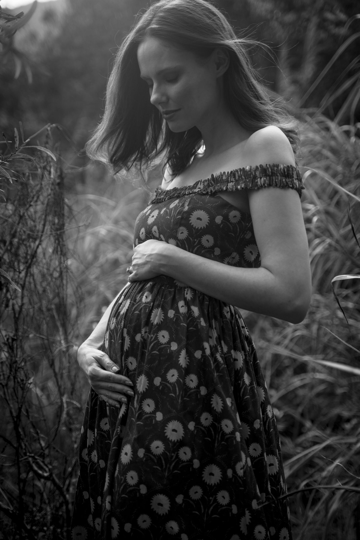 Black and white maternity photo session showing floral dress against natural foliage background.