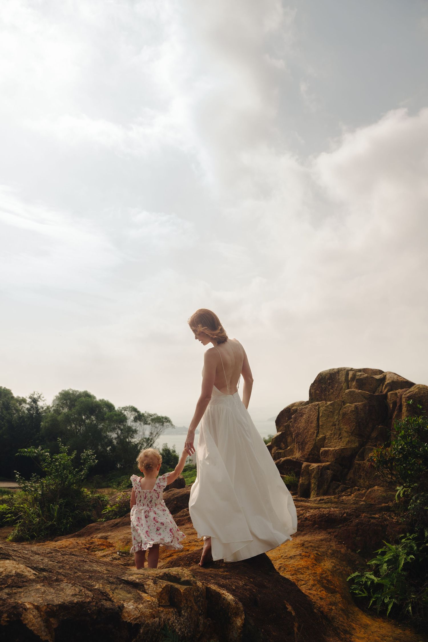 Silhouettes stand on dramatic rocky outcrop against cloudy sky in elegant flowing dresses.