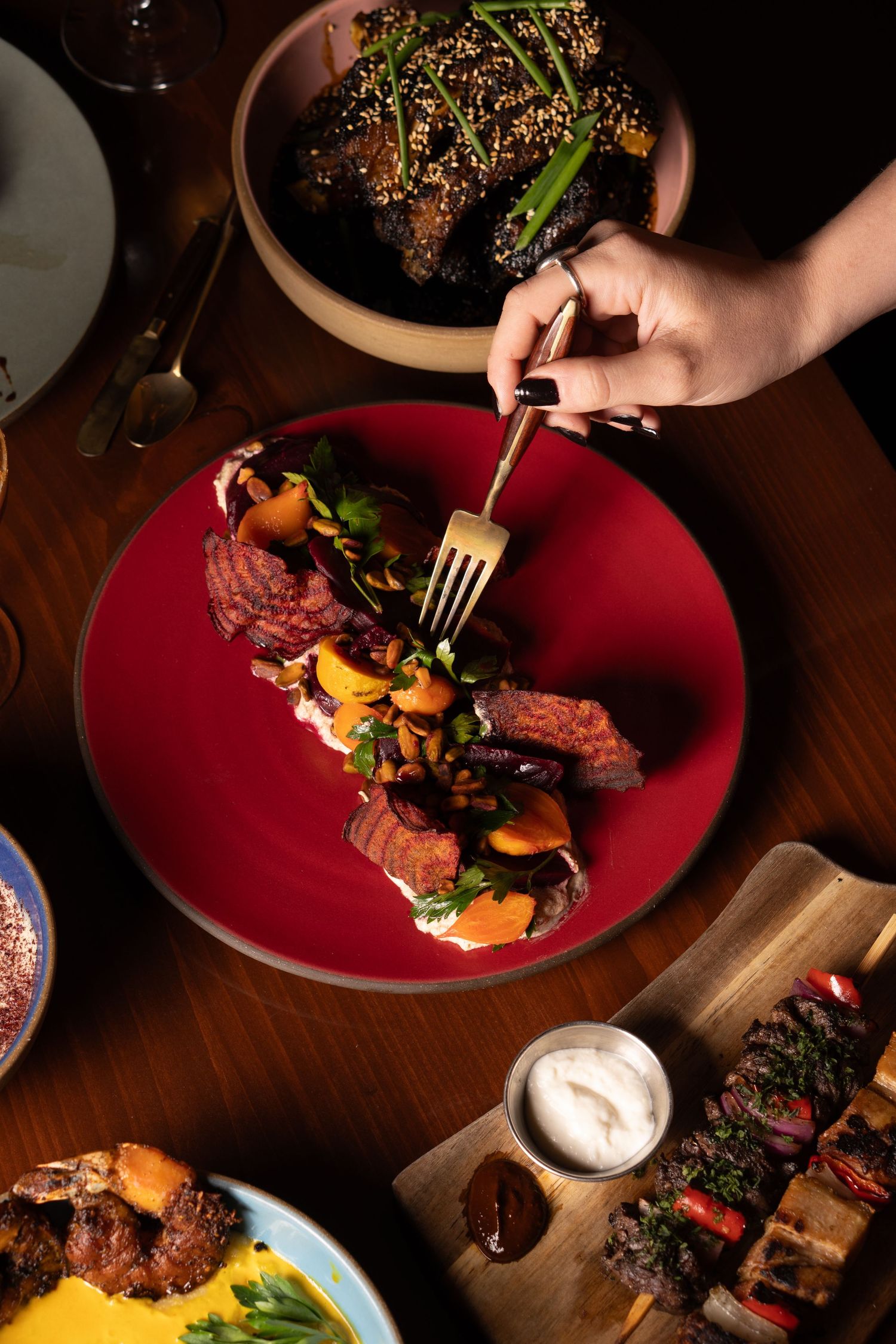 Grilled steak dinner served on red plates with roasted vegetables and creamy sauce on a dark wooden table.