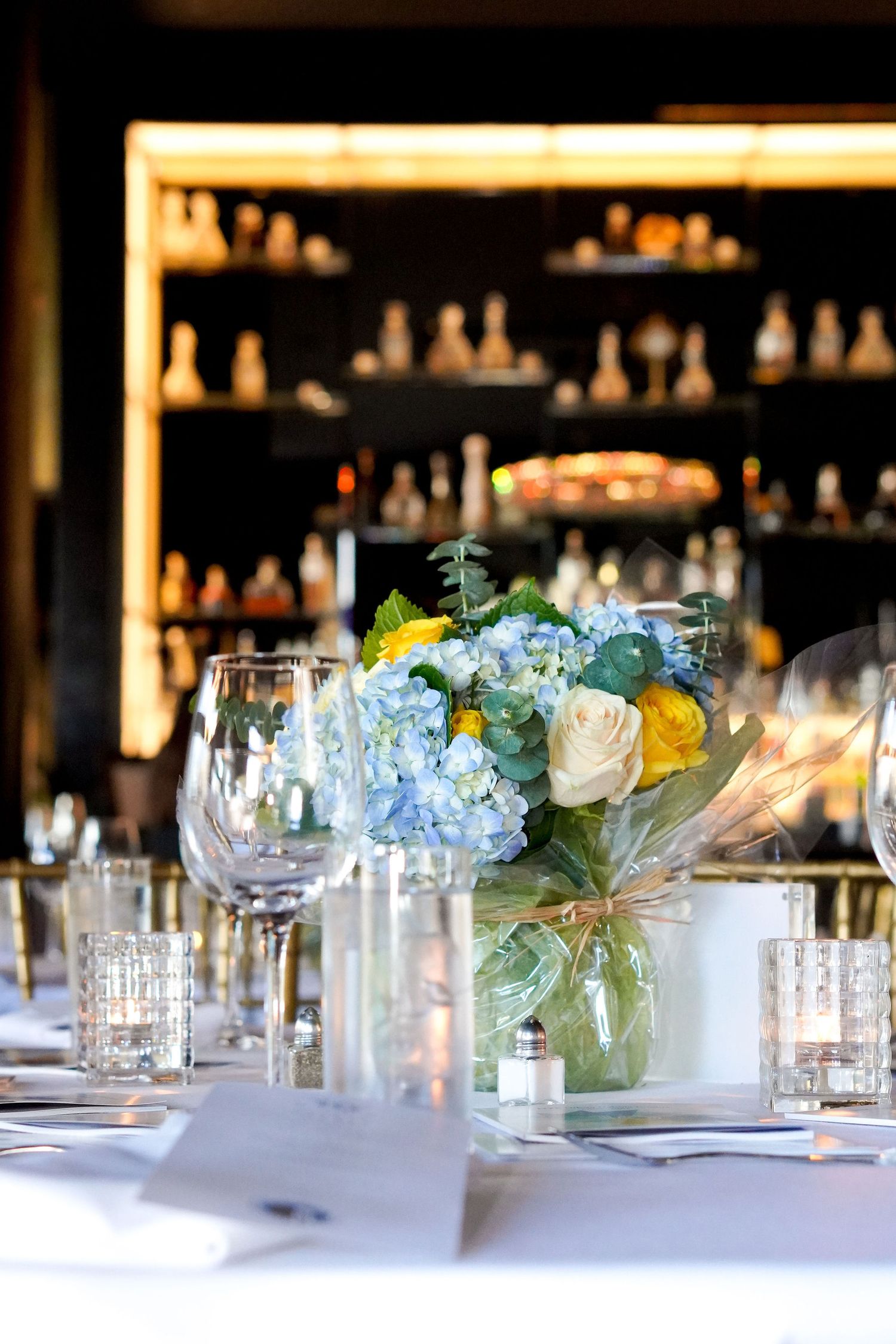 Elegant table setting with blue and yellow floral centerpiece in glass vase at restaurant bar.