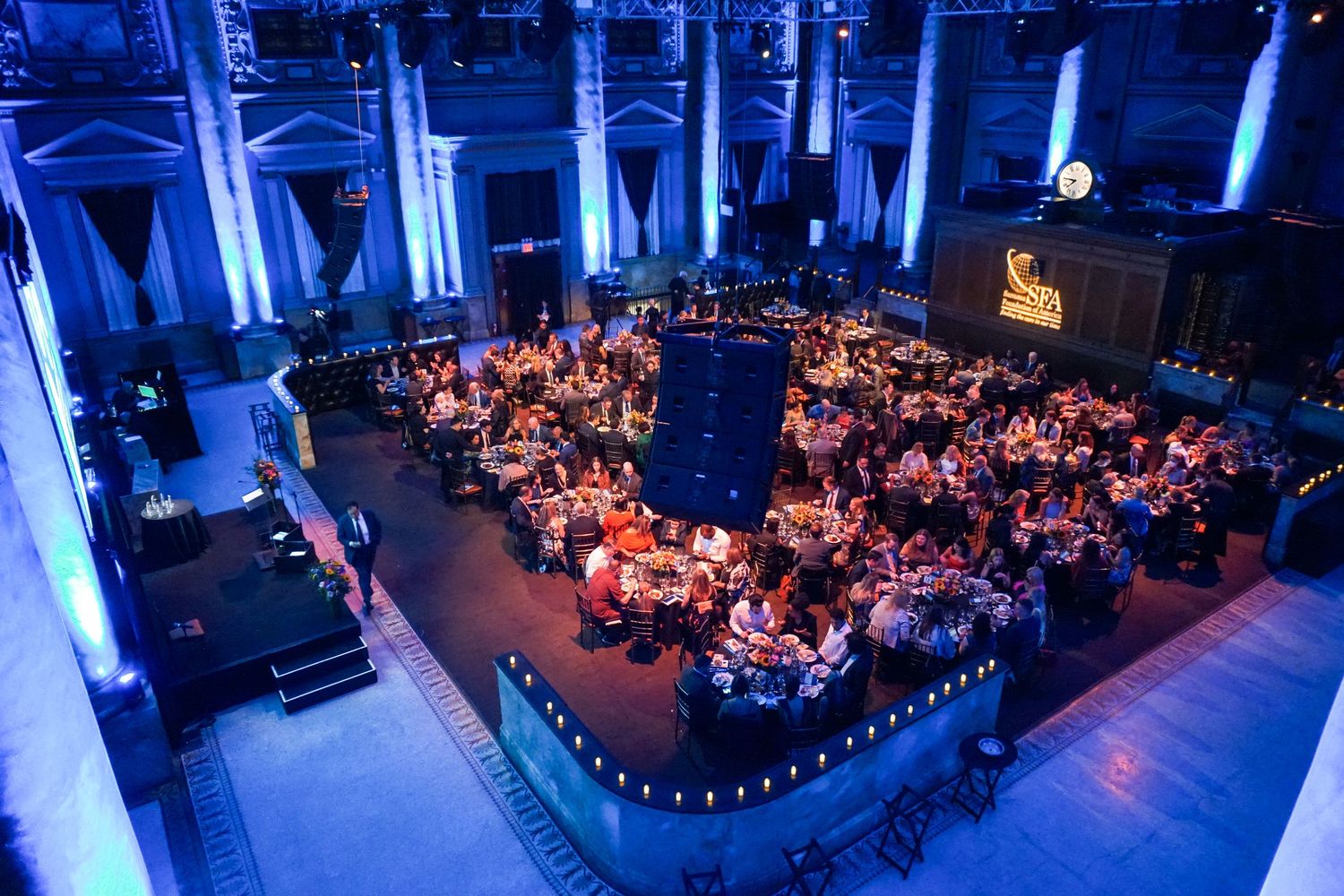 Panoramic view of a grand ballroom with blue lighting and tables set for a formal dinner event.