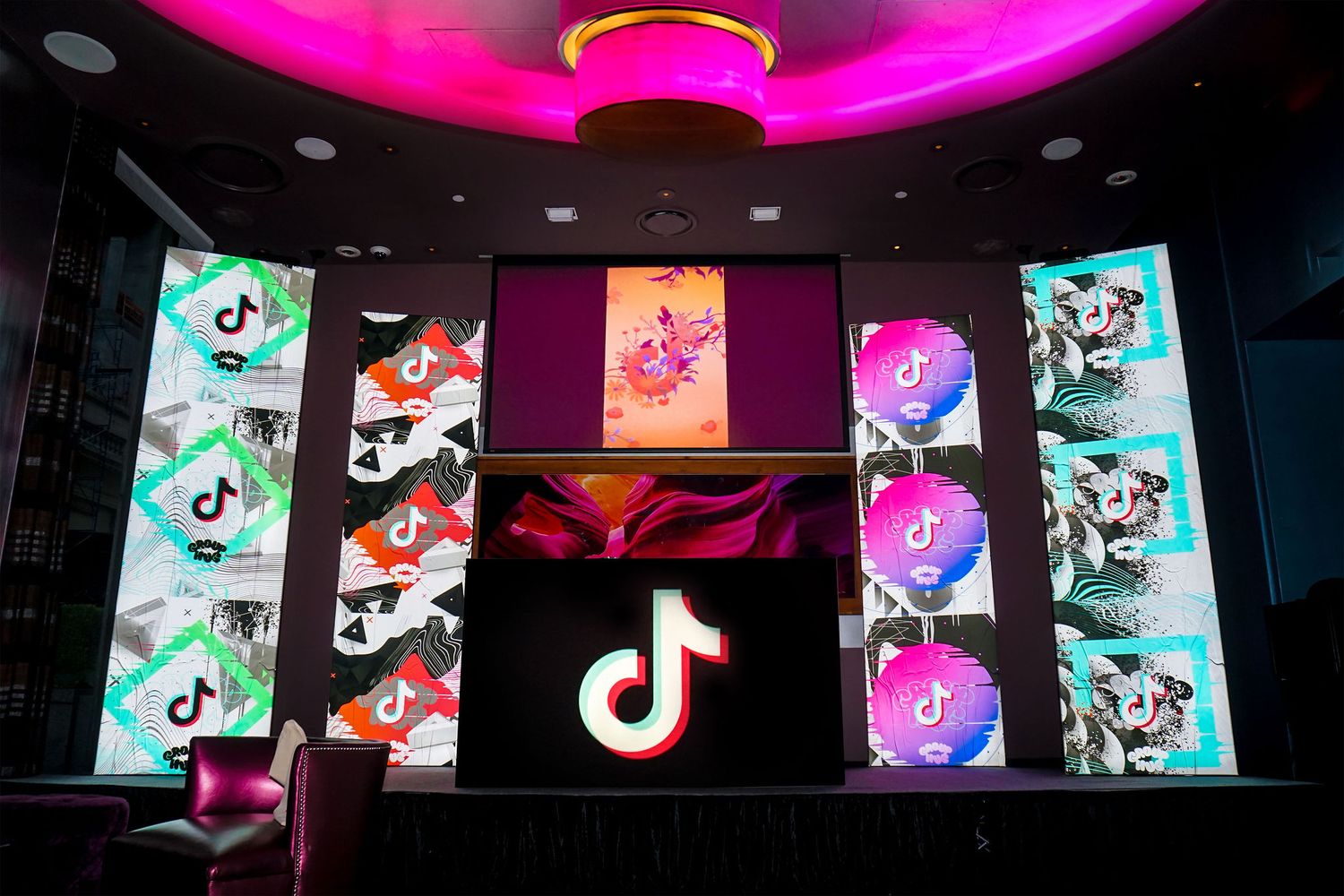 TikTok logo displayed on digital screens with pink ambient lighting at corporate event.