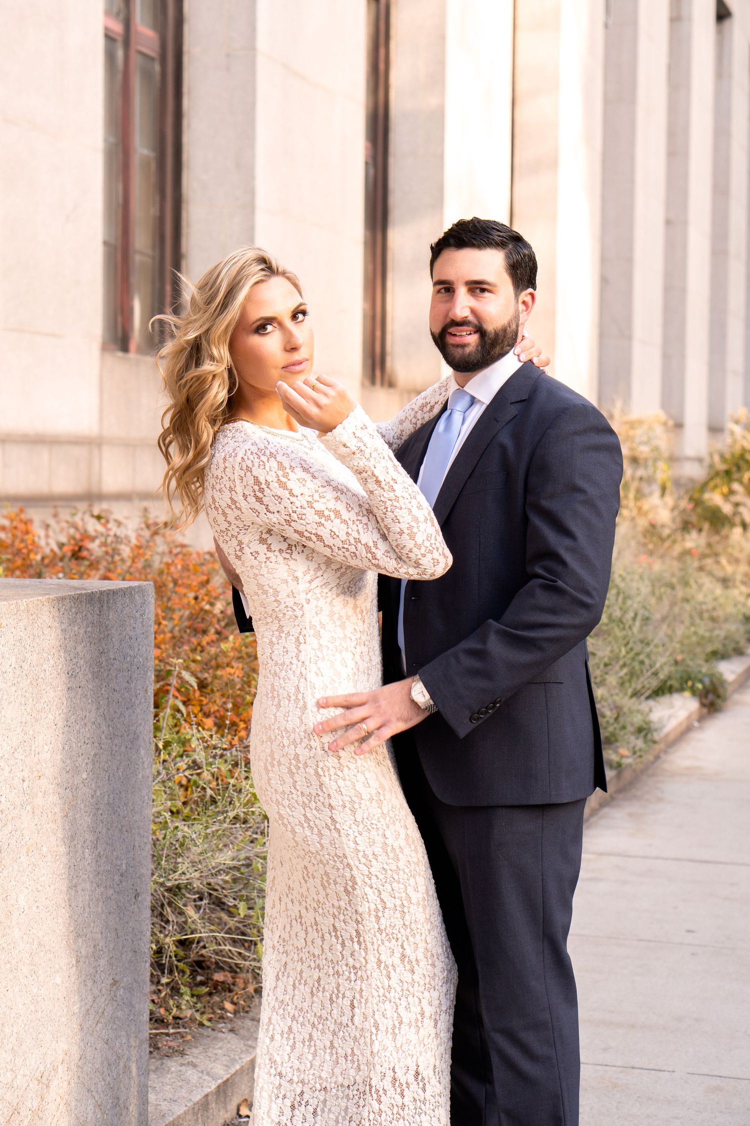 A formal couple poses together outdoors in elegant attire.
