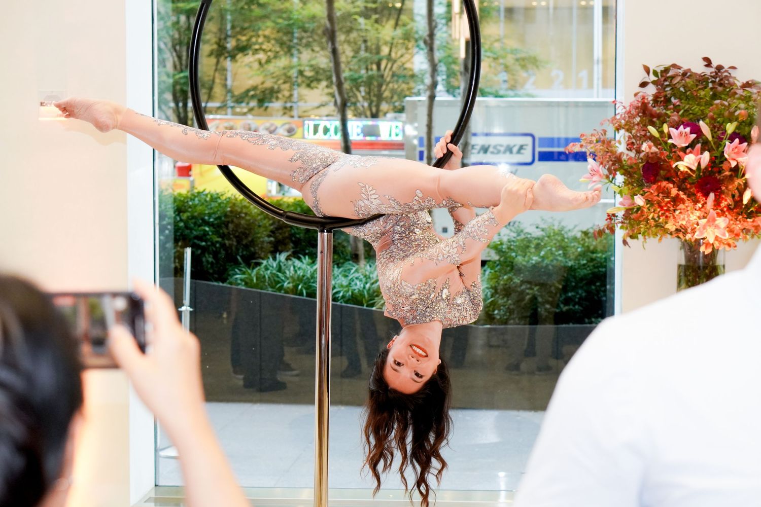 An acrobatic performer does an inverted pose on a pole during an indoor performance.