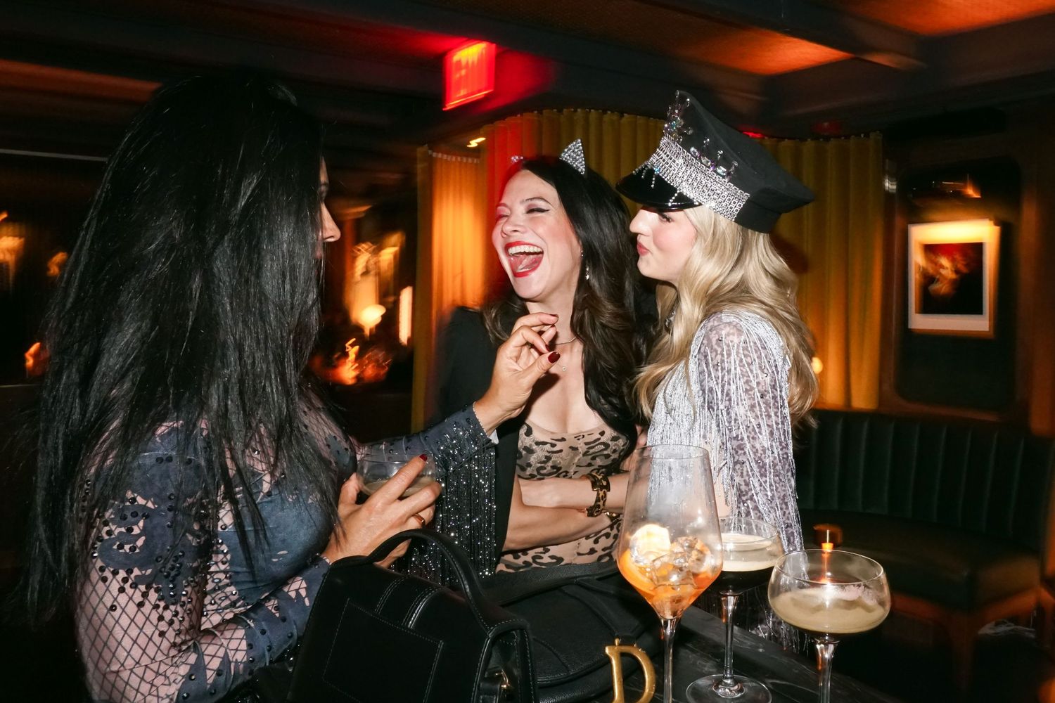 Friends laughing and socializing at a dimly lit bar with cocktails.