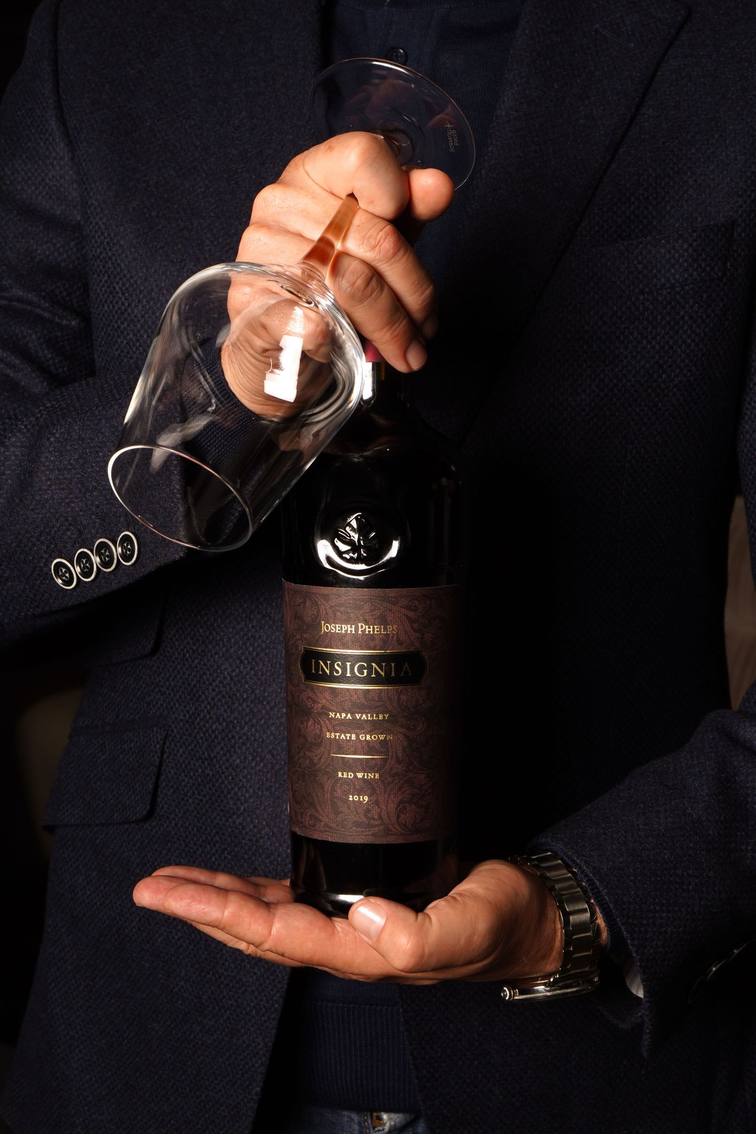 Person in suit holding Joseph Phelps Insignia Napa Valley red wine bottle and empty wine glass.