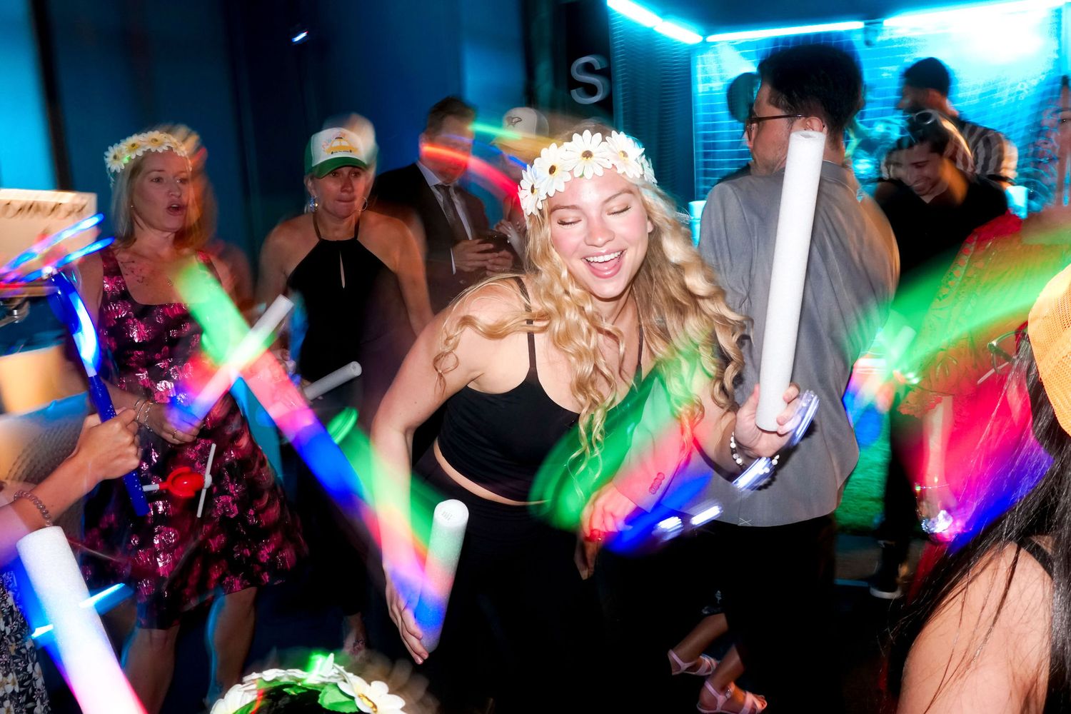 Party crowd dancing with colorful LED light sticks in nightclub atmosphere.