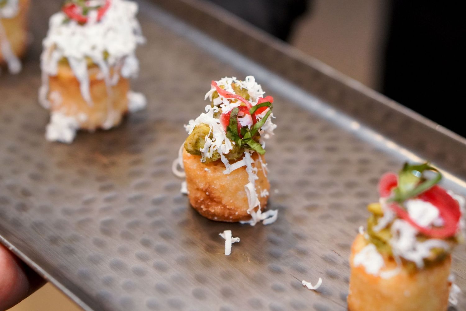 Gourmet appetizer bites garnished with microgreens served on textured metal tray.