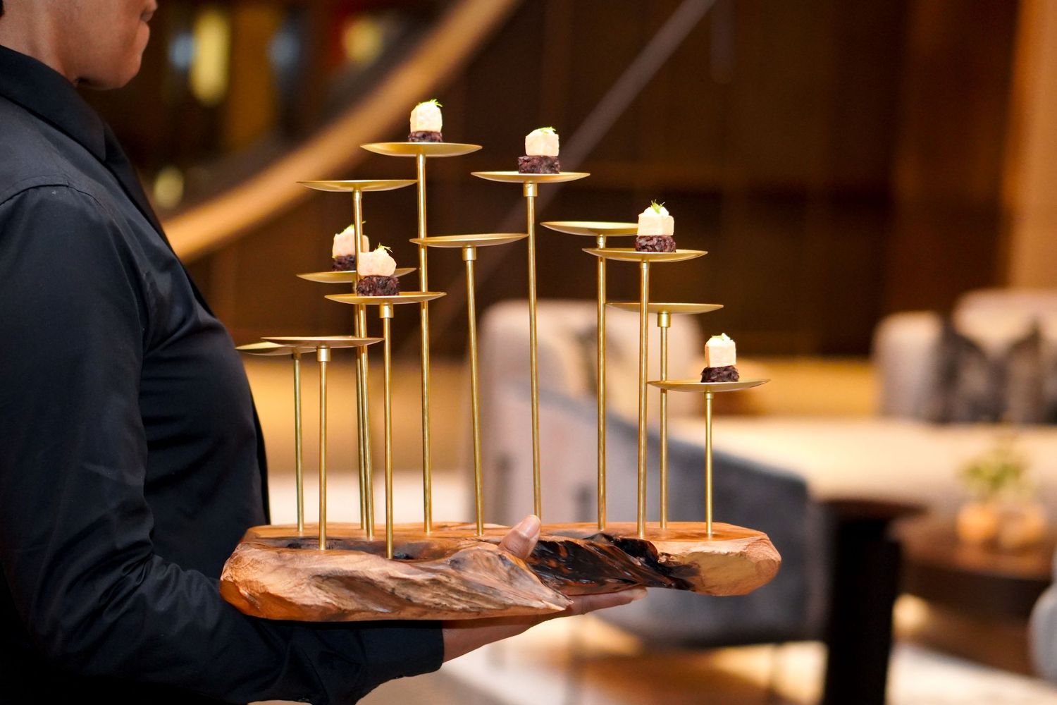 Server holding wooden board with multiple lit candles in geometric arrangement.