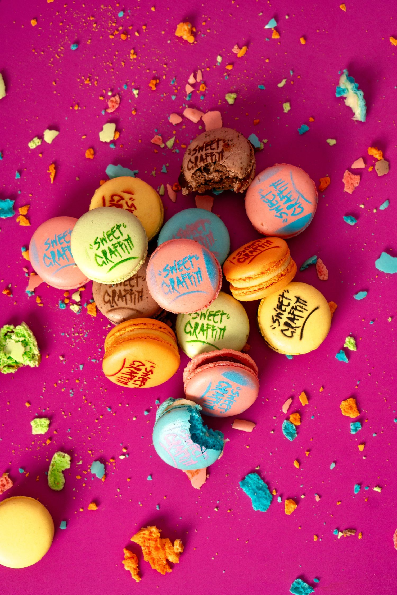Scattered macarons with text and colorful crumbs on bright pink background.