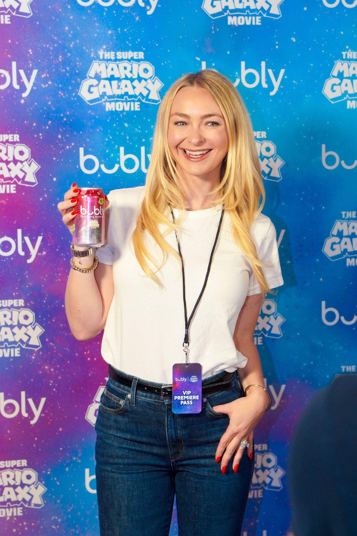Smiling blonde woman holding a Bubly sparkling water can at The Super Mario Galaxy Movie premiere event.