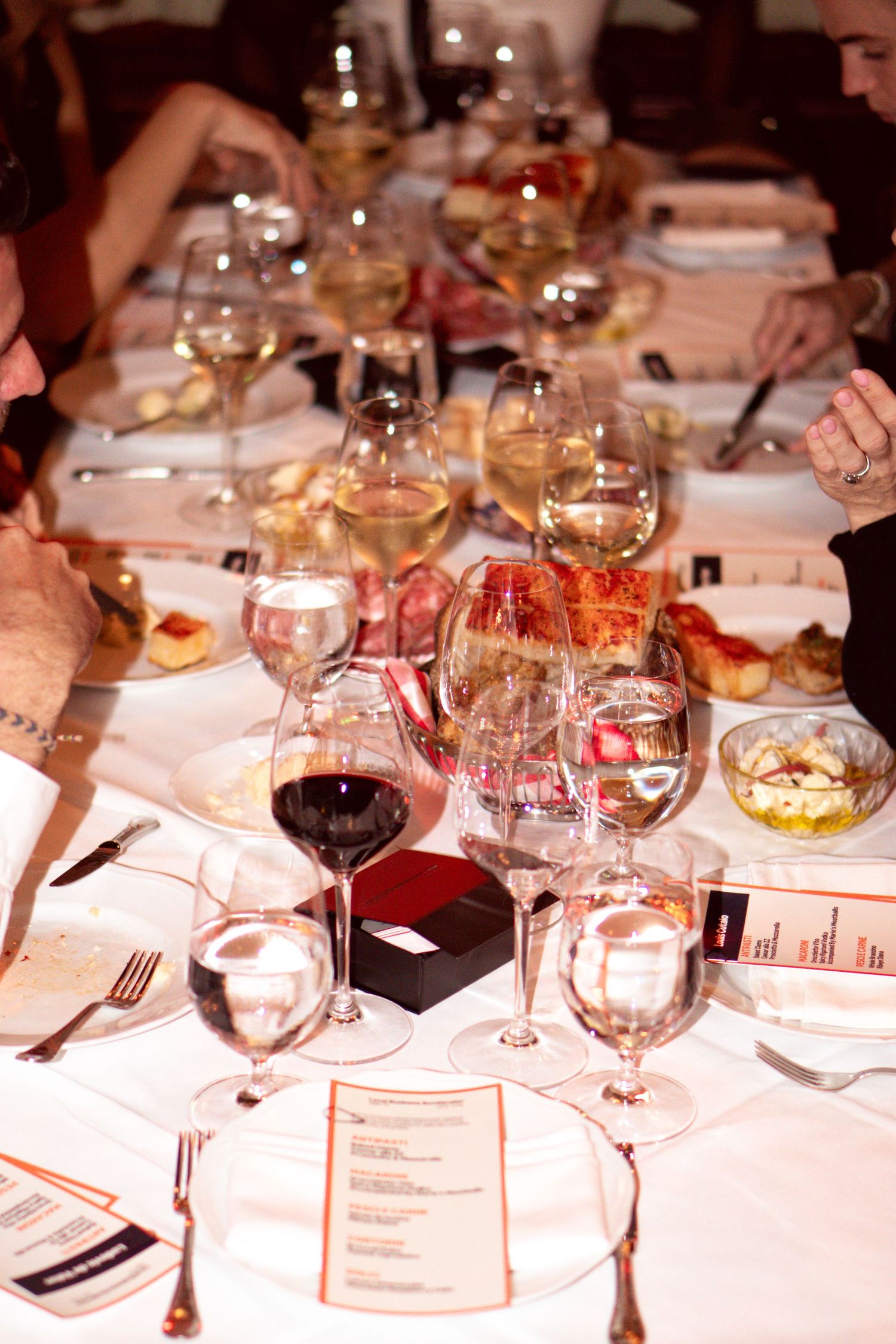 Elegant dinner table set with multiple wine glasses, red and white wines, menus, and gourmet dishes at a formal event.