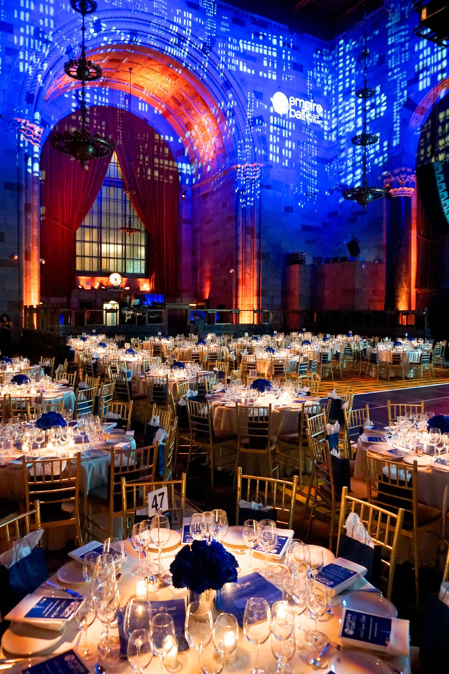 Elegant grand ballroom gala with blue lighting, gold chiavari chairs, and round tables set for a formal dinner event.