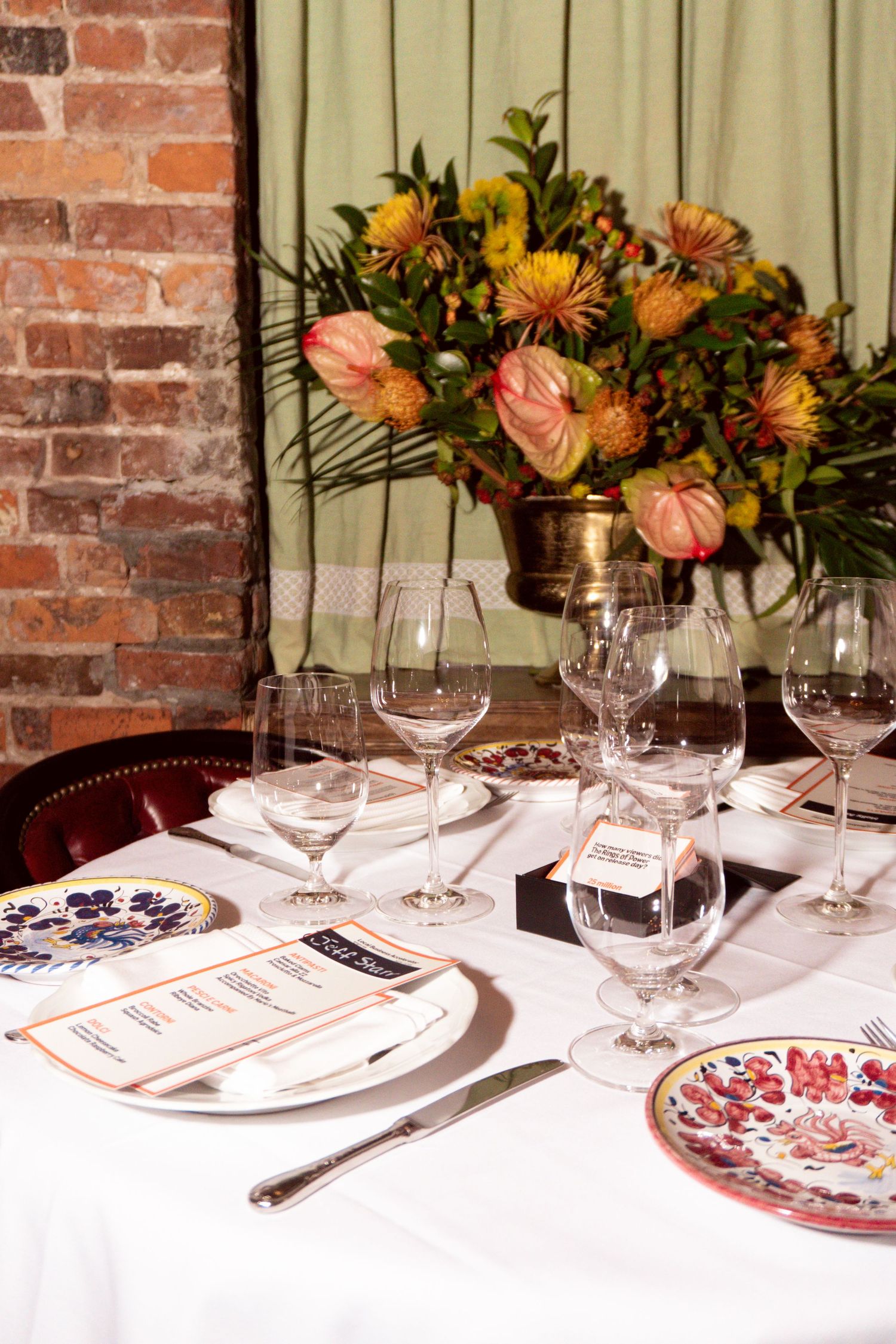 Elegant restaurant table setting with floral centerpiece, wine glasses, decorative plates, and menus on white tablecloth.