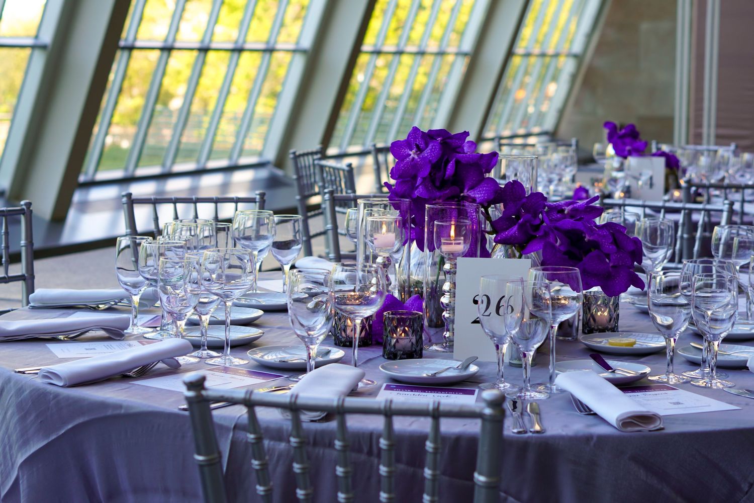 Elegant table setting with purple orchid centerpieces and silver chiavari chairs.
