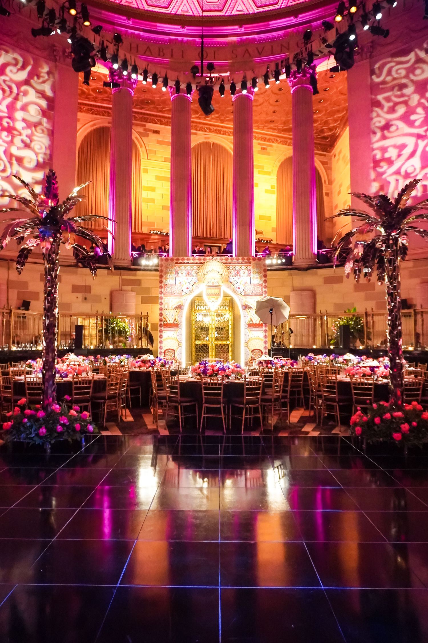Luxurious ballroom with pink lighting, columns and elegant table settings for formal event.