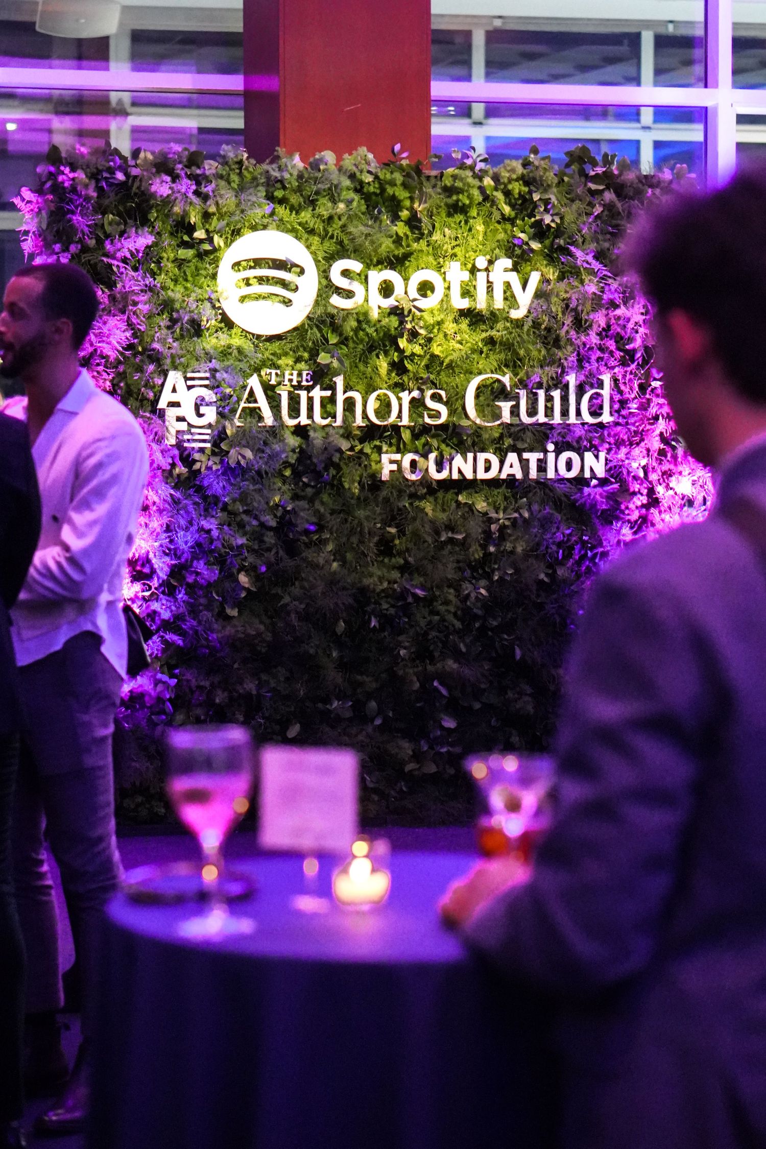 Spotify and Authors Guild Foundation logos illuminated with purple lighting at an event venue with floral decor.