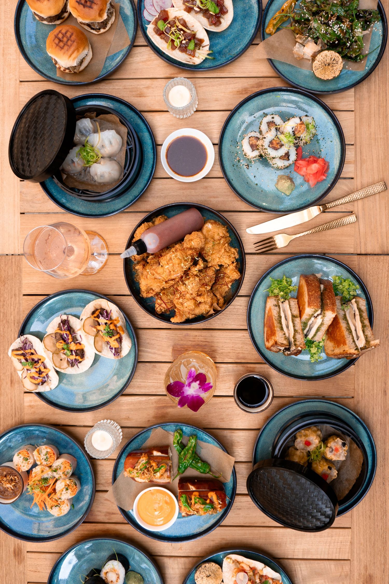 Overhead view of various Asian dishes served on blue plates on wooden table.
