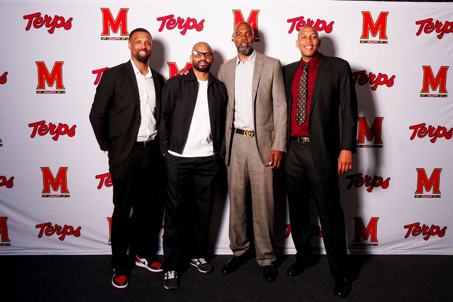 Four men posing together at a University of Maryland Terps event backdrop wearing formal attire.