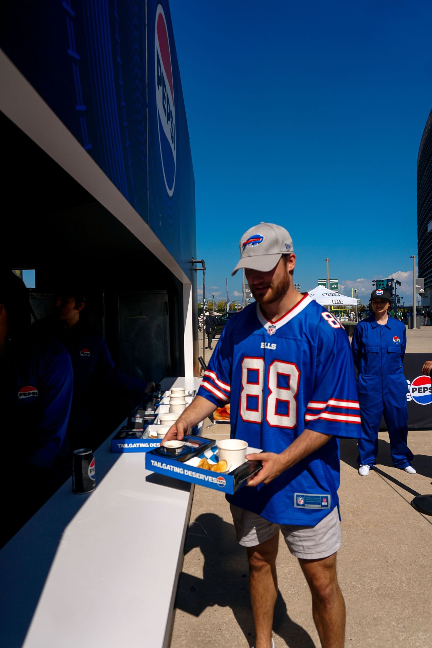 Buffalo Bills fan in #88 jersey at Pepsi promotional booth outside stadium on a sunny game day.