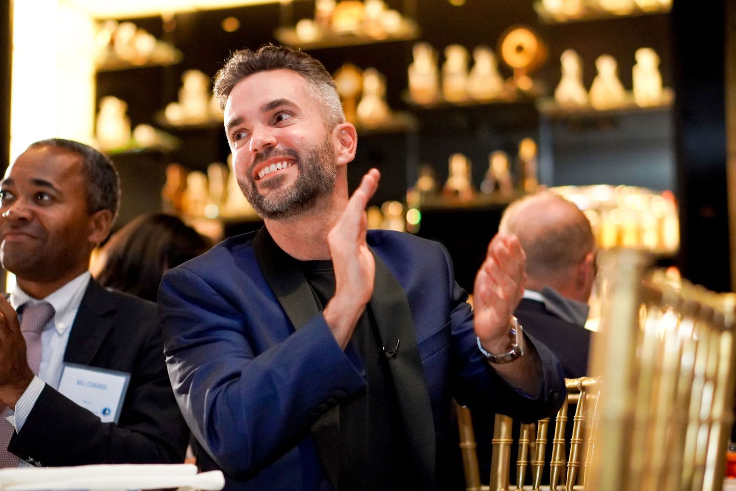 Men in formal attire applaud during an elegant evening event at an upscale bar.