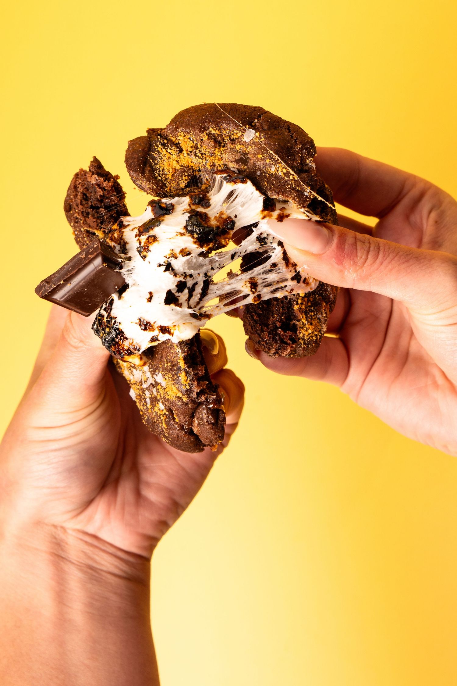 Chocolate cookie being pulled apart revealing marshmallow filling against yellow background.