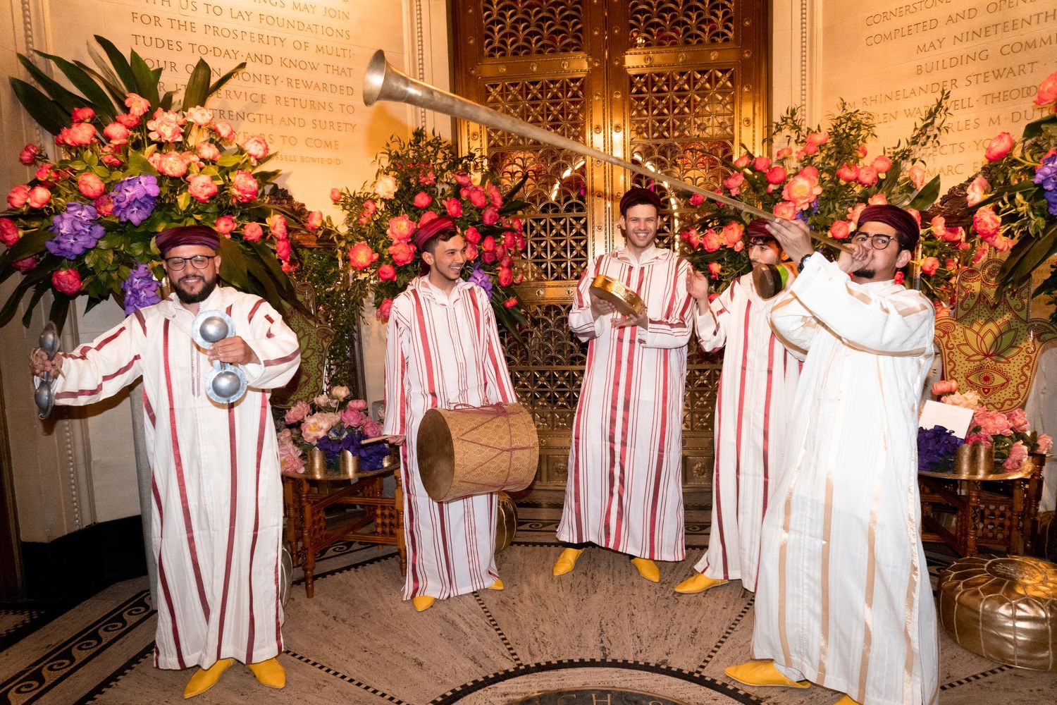 Group performance in white robes against a backdrop of floral arrangements and warm lighting.
