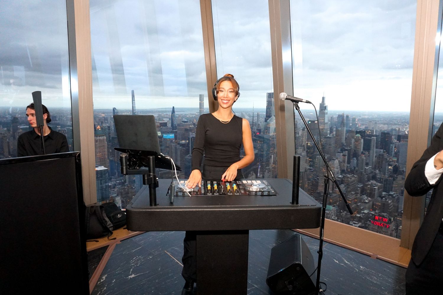 DJ performing at a high-rise venue with panoramic city skyline views.