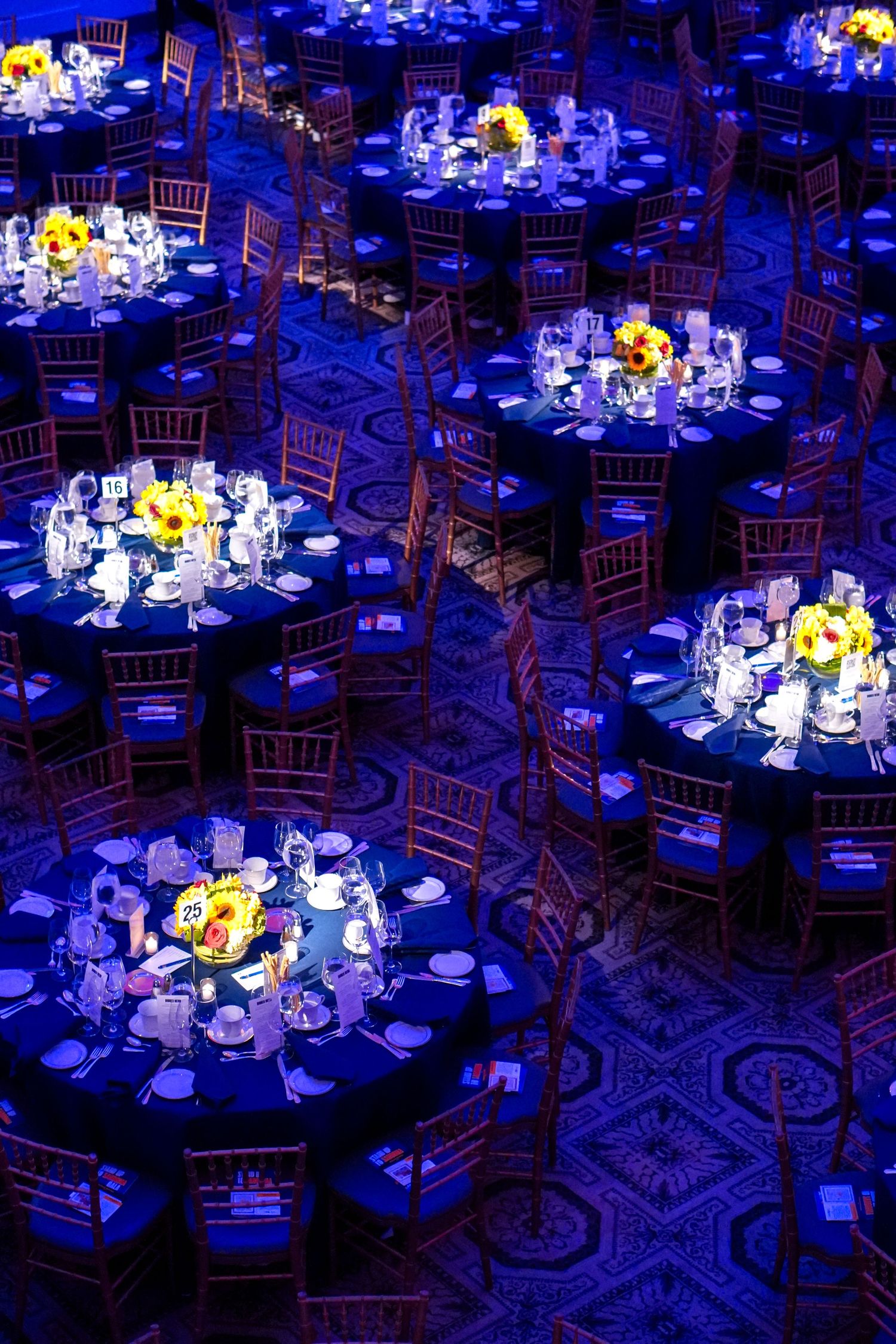 Elegant banquet hall setup with round tables under dramatic blue lighting and floral centerpieces.