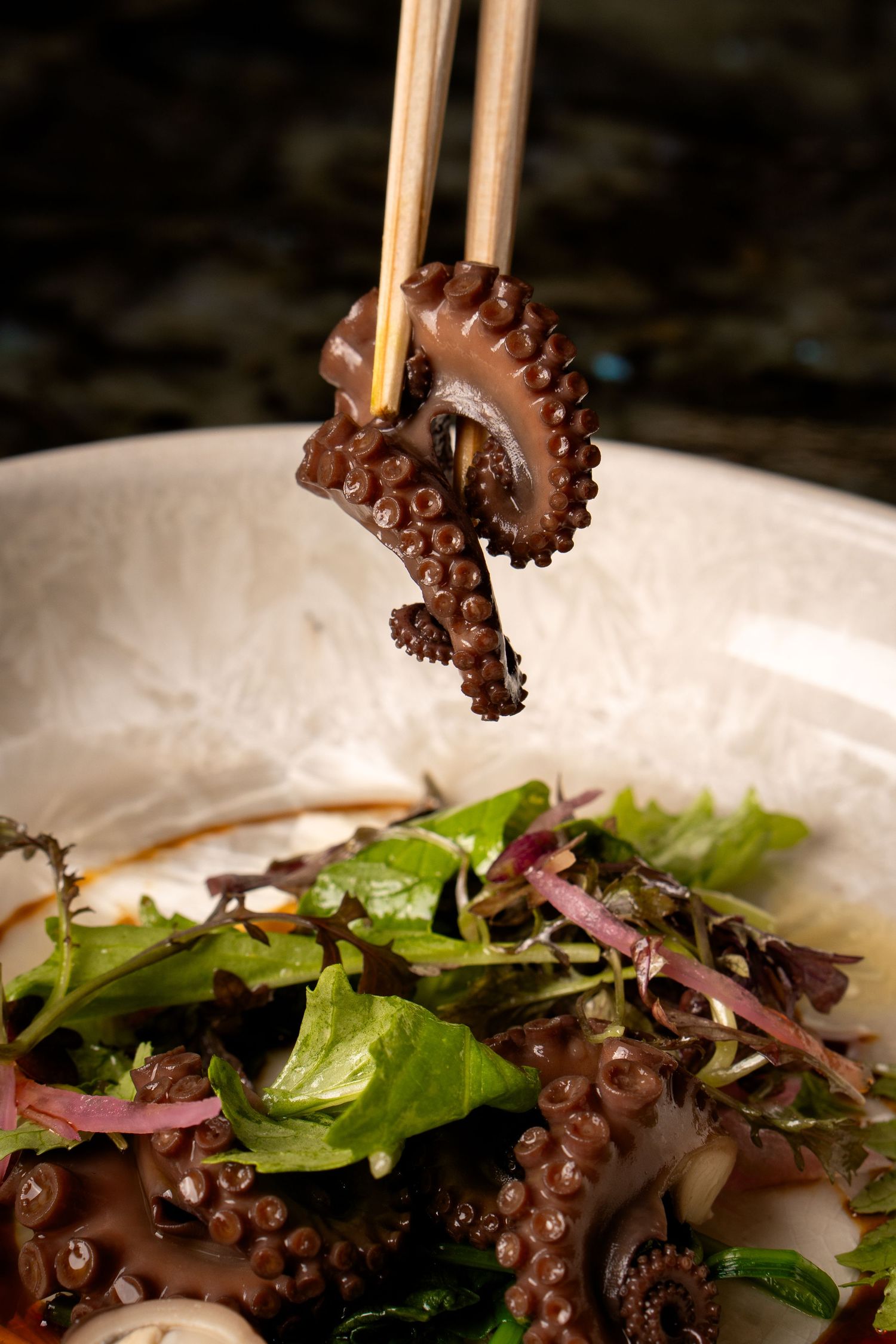 Fresh octopus tentacles with greens being picked up by chopsticks.