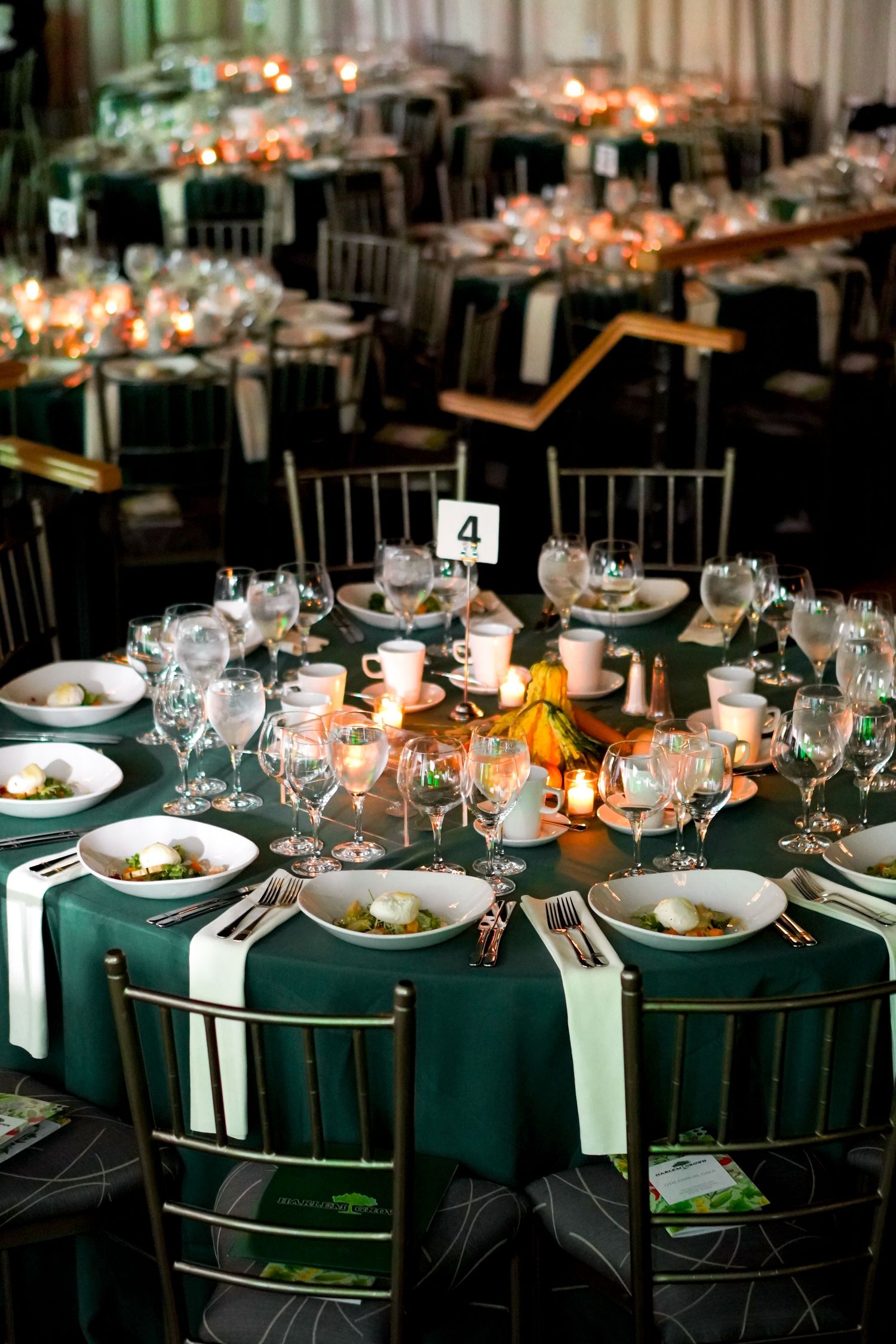 Formal dining tables set with dark green linens, white plates, and glowing candlelight for an upscale event.