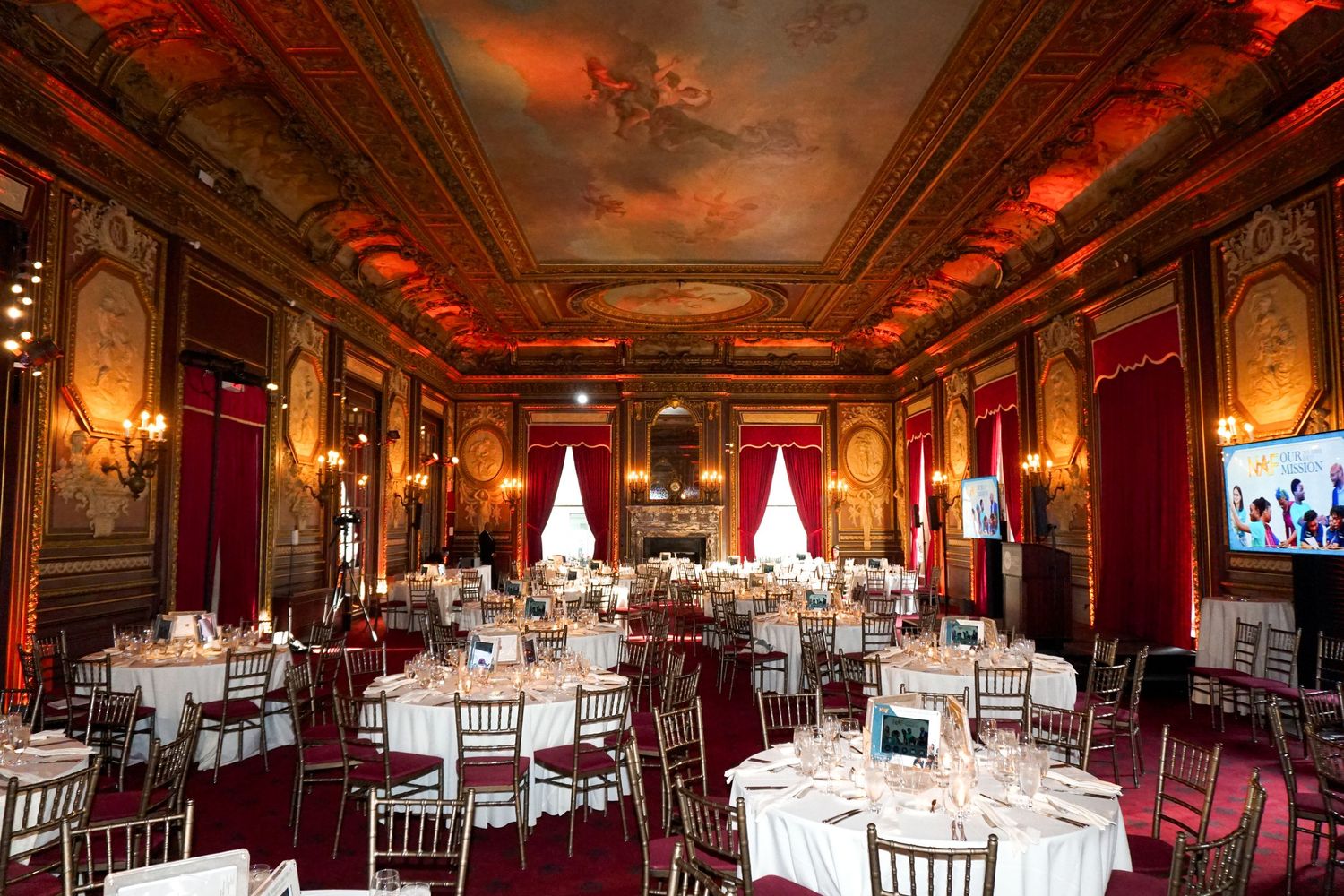 Grand ballroom with red velvet curtains, ornate ceiling murals, and formal table settings.